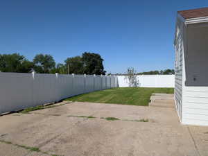 Expansive backyard featuring a white privacy fence, manicured lawn, concrete patio area, and white siding exterior