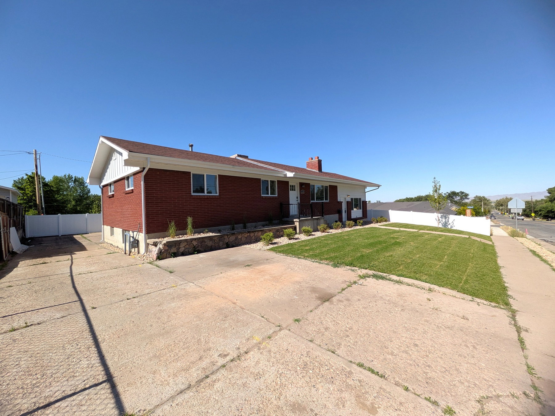 Brick exterior residence featuring a white vinyl fence, established front lawn, and concrete driveway