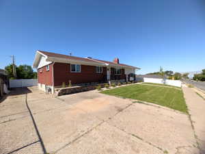 Brick exterior residence featuring a white vinyl fence, established front lawn, and concrete driveway
