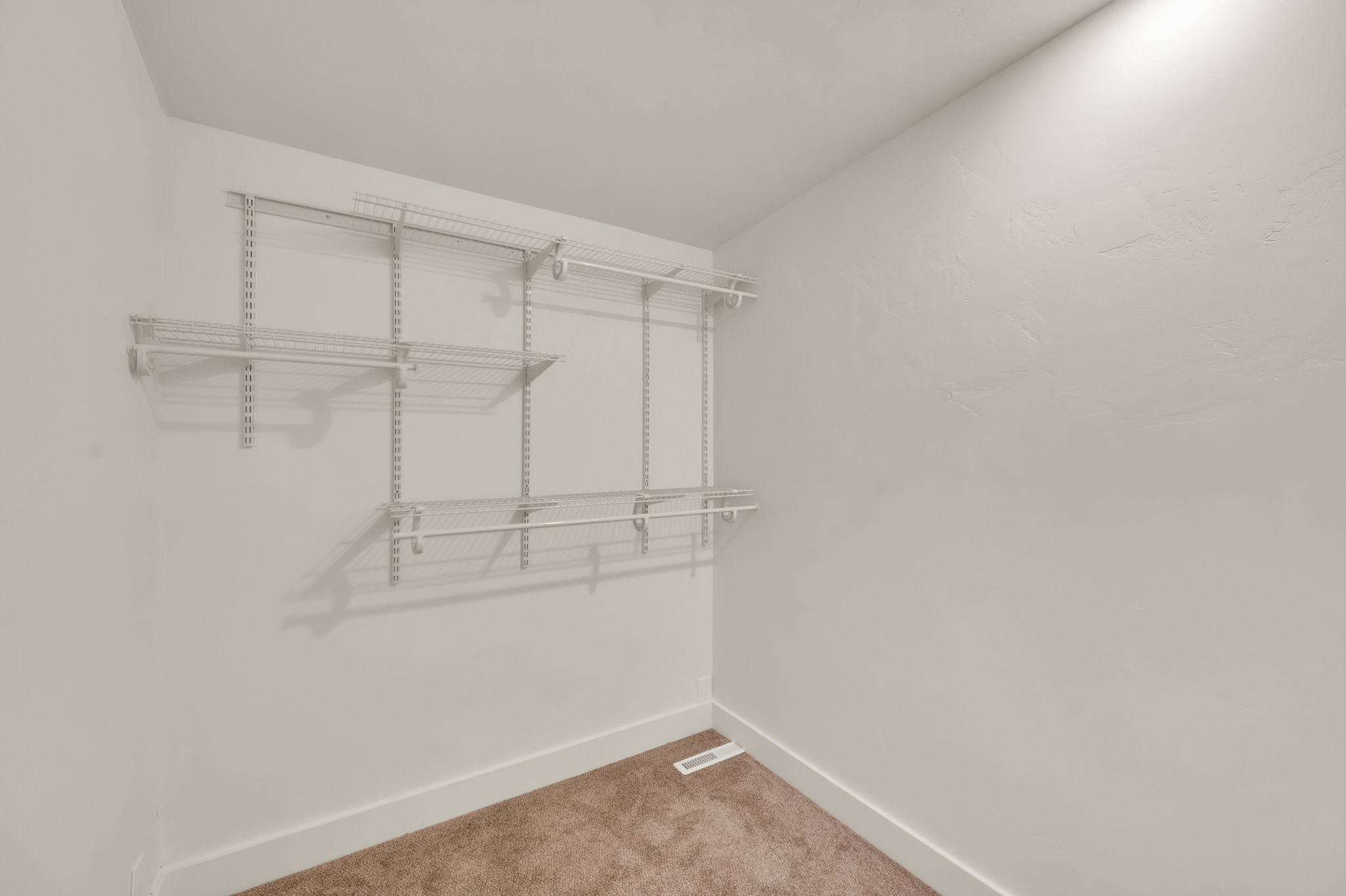 Walk-in closet featuring adjustable wire shelving, multiple hanging rods, white walls, white baseboards, and brown carpet flooring