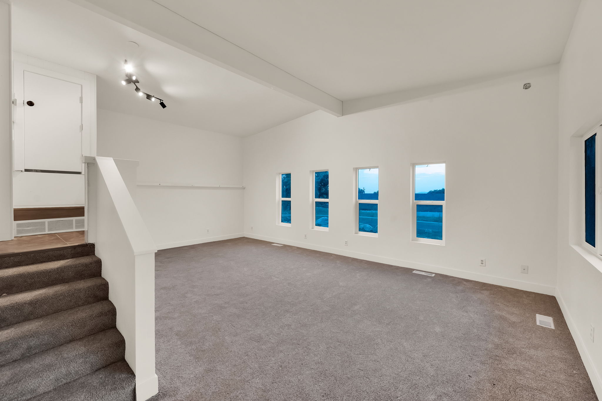 Spacious room featuring vaulted ceilings, track lighting, neutral wall finishes, carpeted flooring, and multiple windows