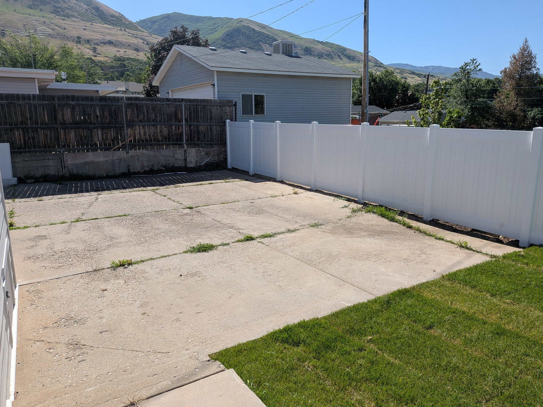 Paved concrete area featuring a white privacy fence and a section of green lawn
