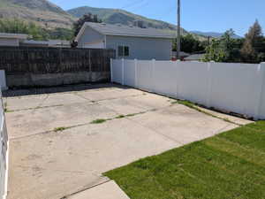 Paved concrete area featuring a white privacy fence and a section of green lawn