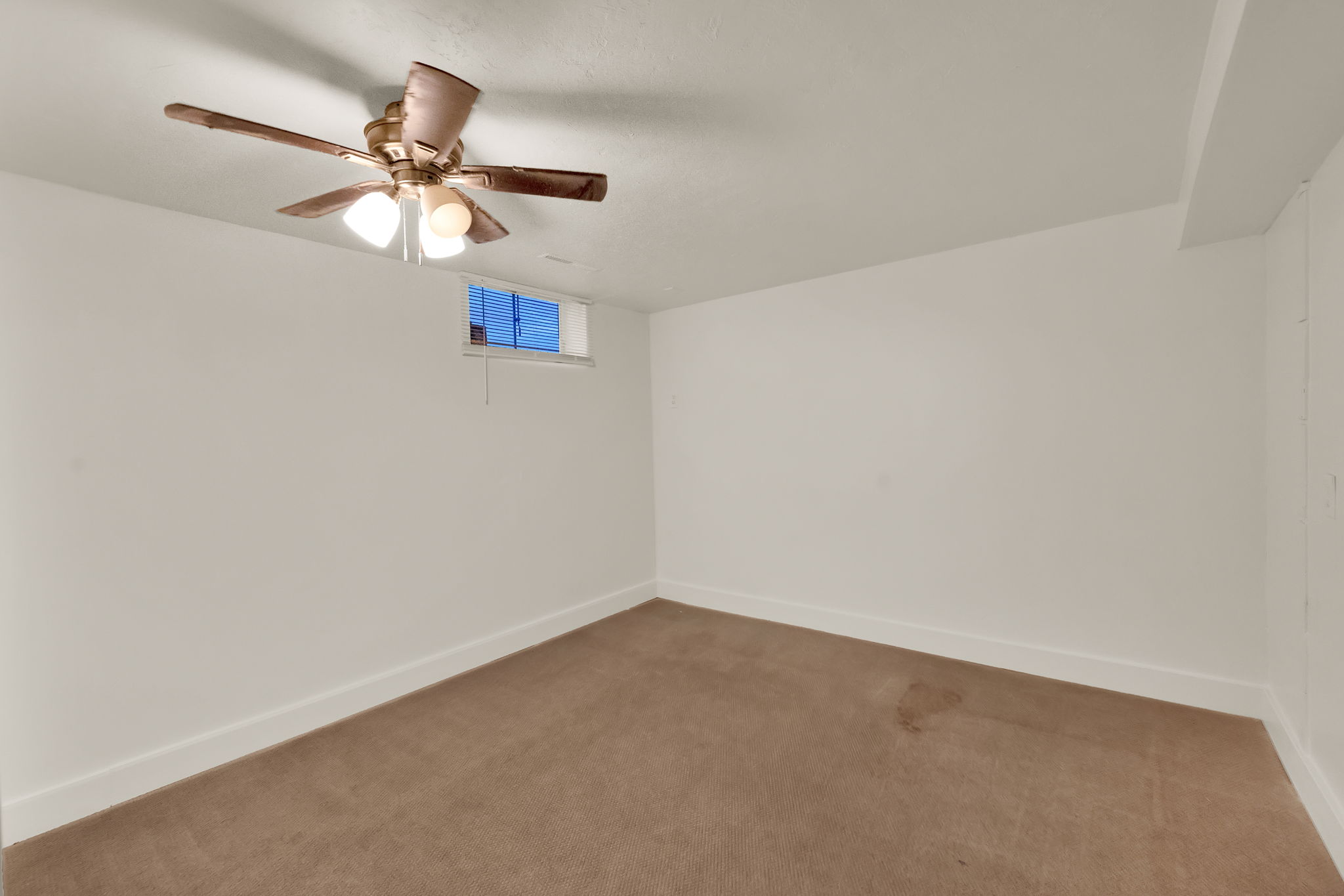 Carpeted room featuring a ceiling fan with integrated lighting, white painted walls, and a small transom window