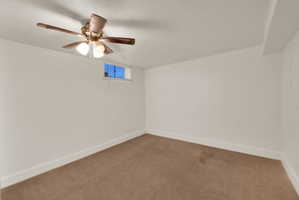 Carpeted room featuring a ceiling fan with integrated lighting, white painted walls, and a small transom window