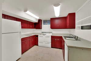 Kitchen featuring red cabinetry, white countertops, white appliances, and a stainless steel sink