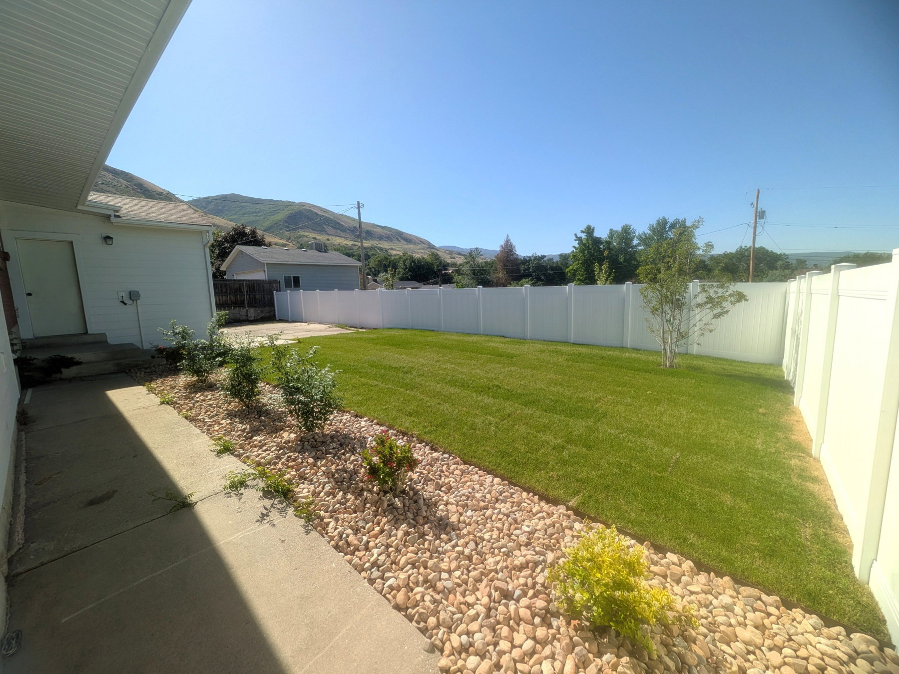 Expansive backyard featuring a lush lawn, white vinyl fencing, and a decorative rock border with plantings