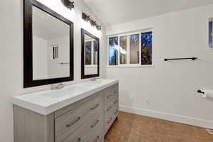 Bathroom featuring a dual vanity with light wood-finish cabinetry, integrated sinks, white countertops, and dark framed mirrors