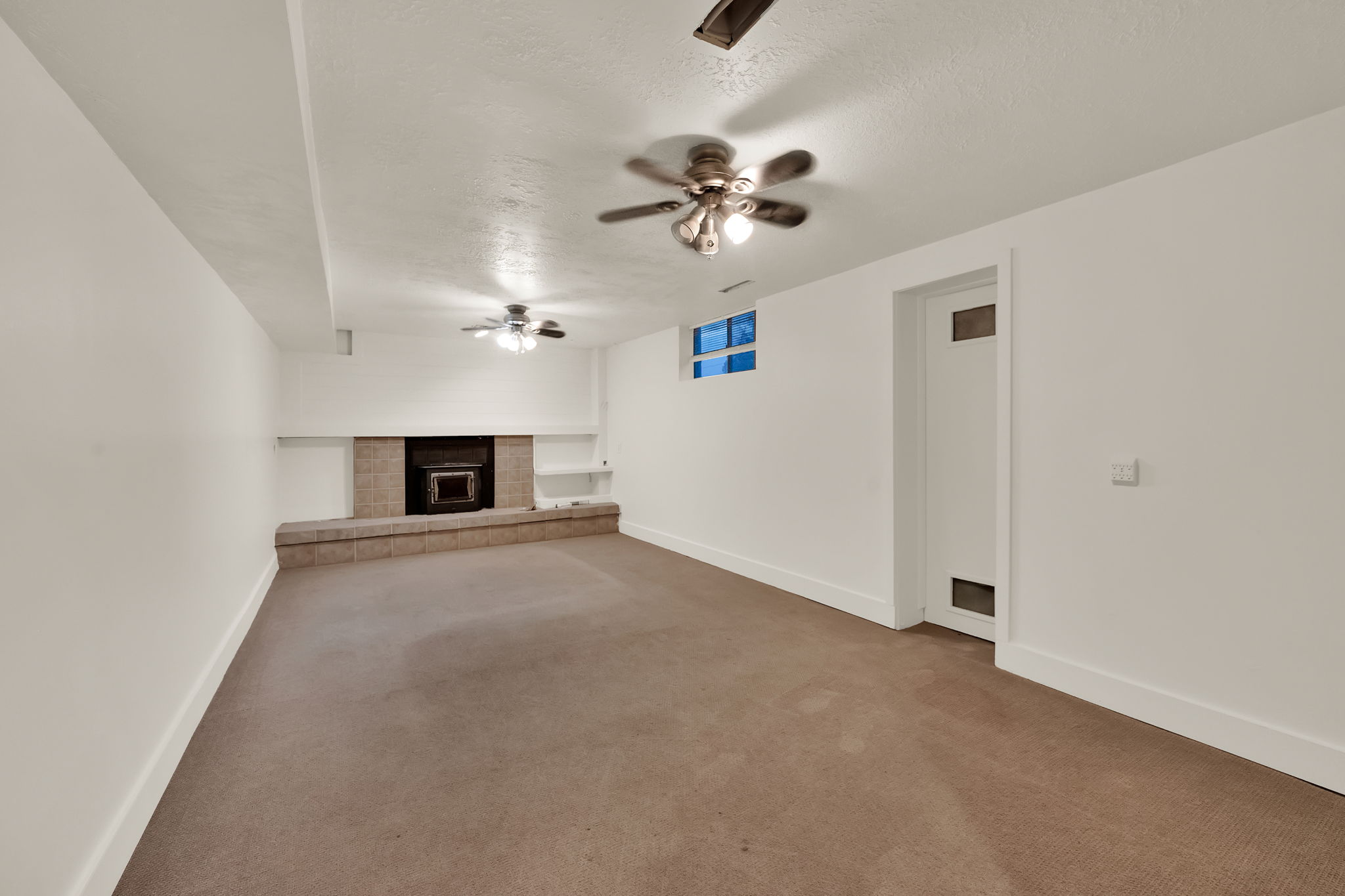 Spacious room featuring a stone fireplace with hearth, integrated shelving, three ceiling fans, and a window