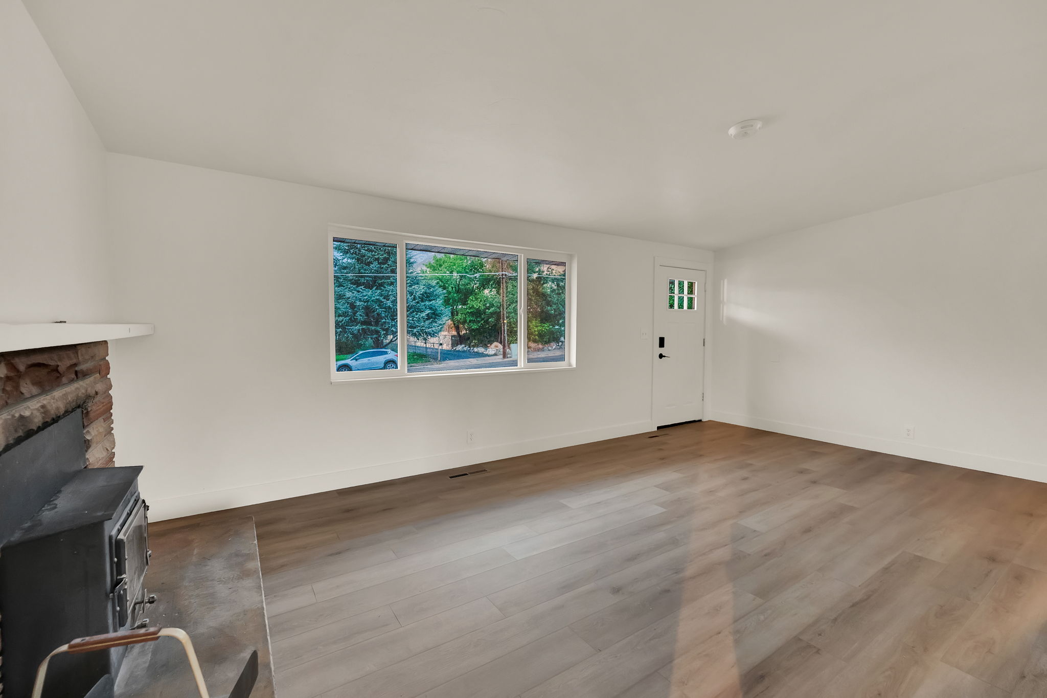 Spacious interior featuring wide plank wood-finish flooring, a stone fireplace with a wood-burning insert, a white mantel, and a multi-pane entry door