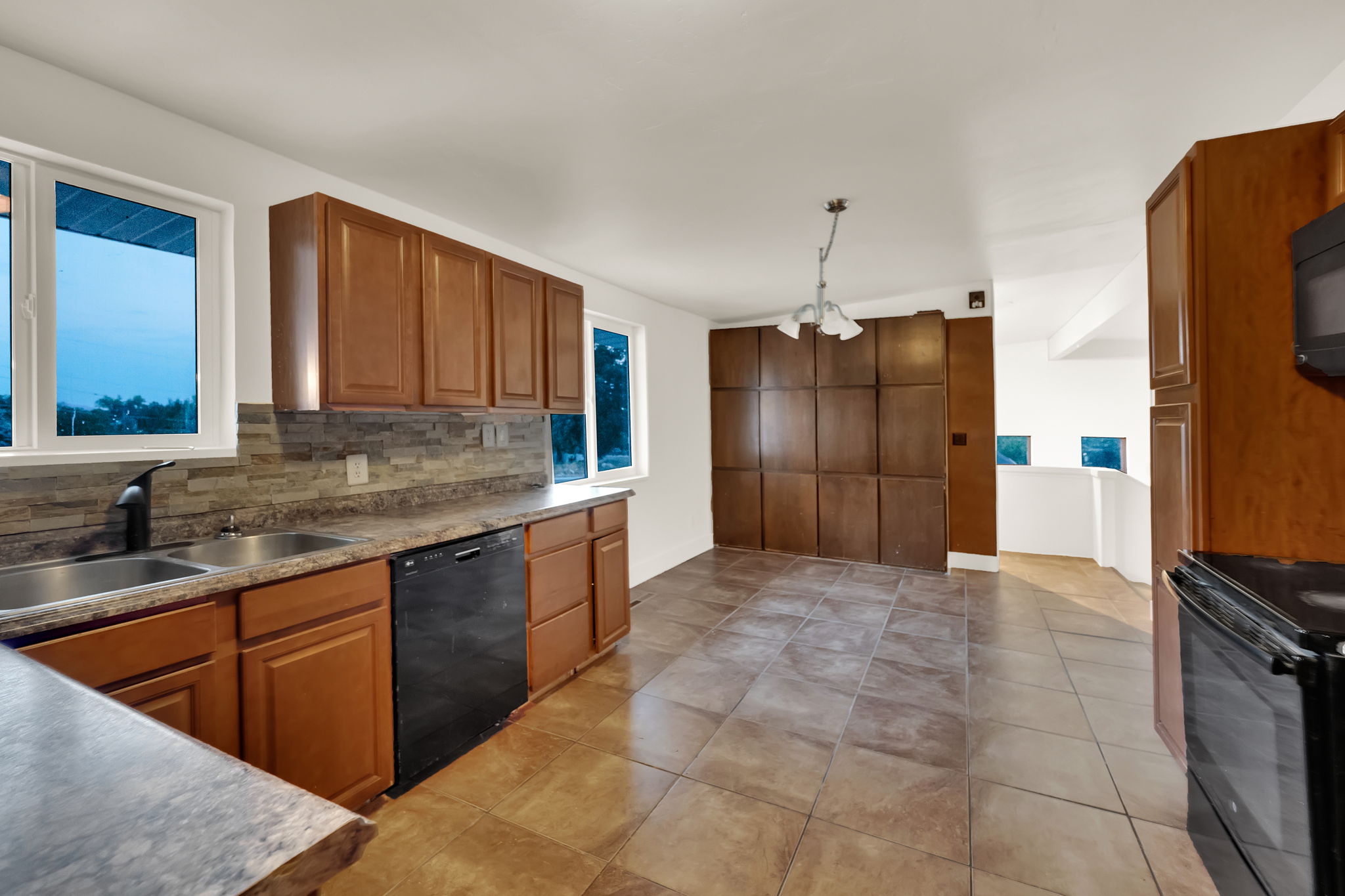 Kitchen featuring wood-finish cabinetry, a double basin stainless steel sink with a matte black faucet, and a stone-tile backsplash