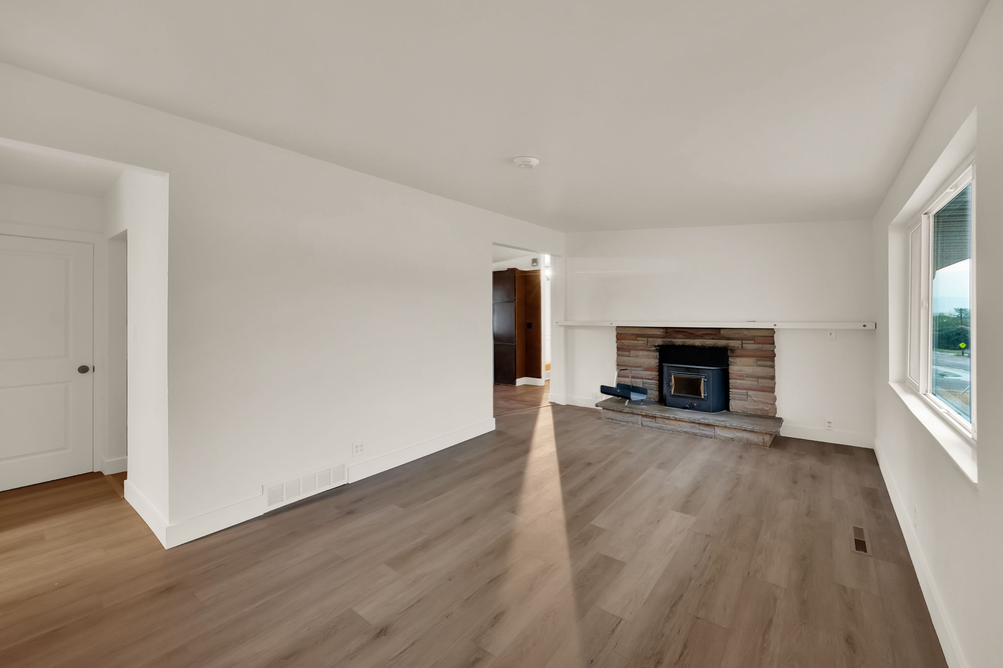Spacious room featuring wood-finish flooring, white baseboards, and a stone-clad fireplace with a dark insert