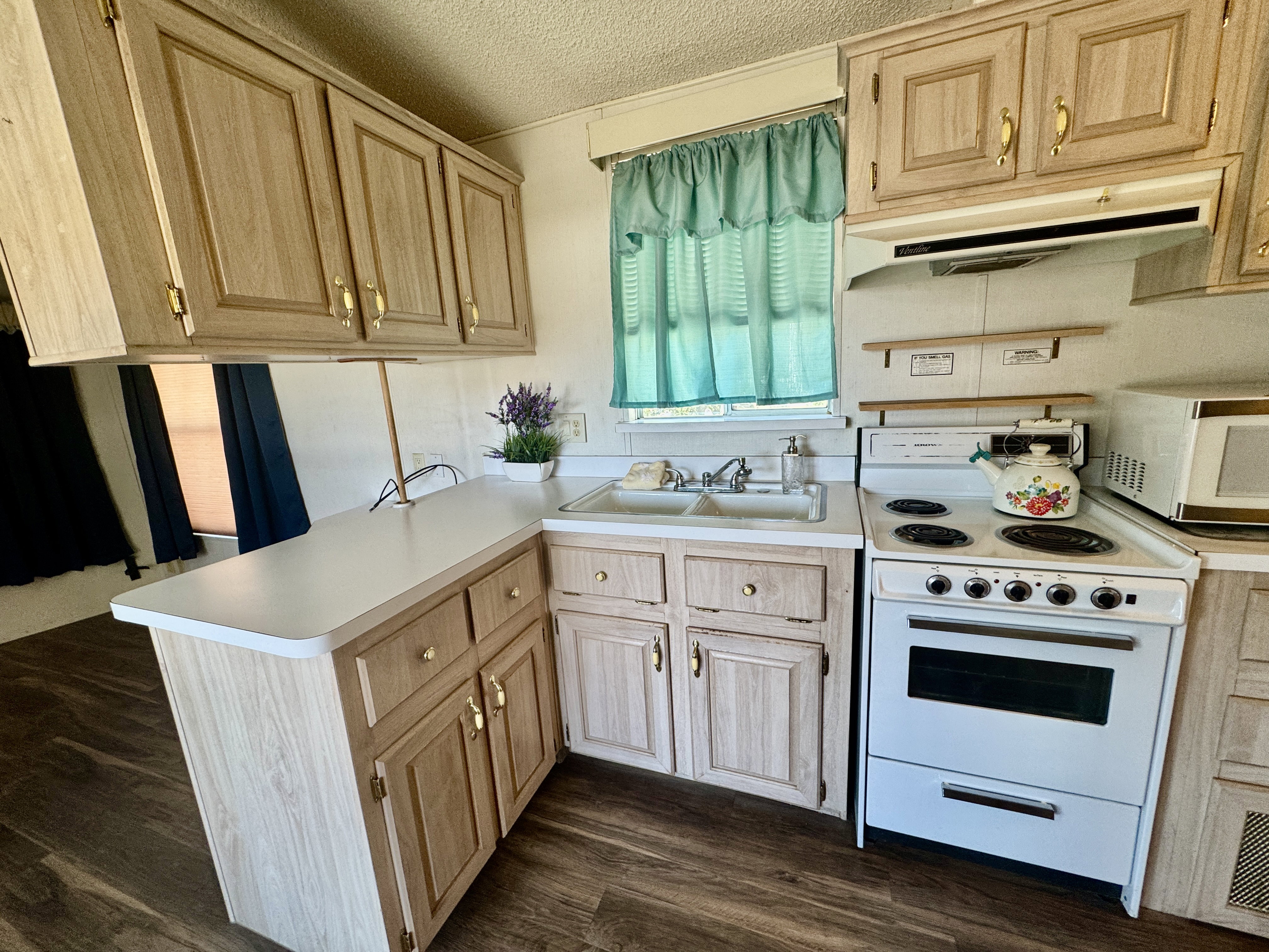 Kitchen featuring wood-finish cabinetry with brass hardware, white countertops, a double basin sink, and wood-finish flooring