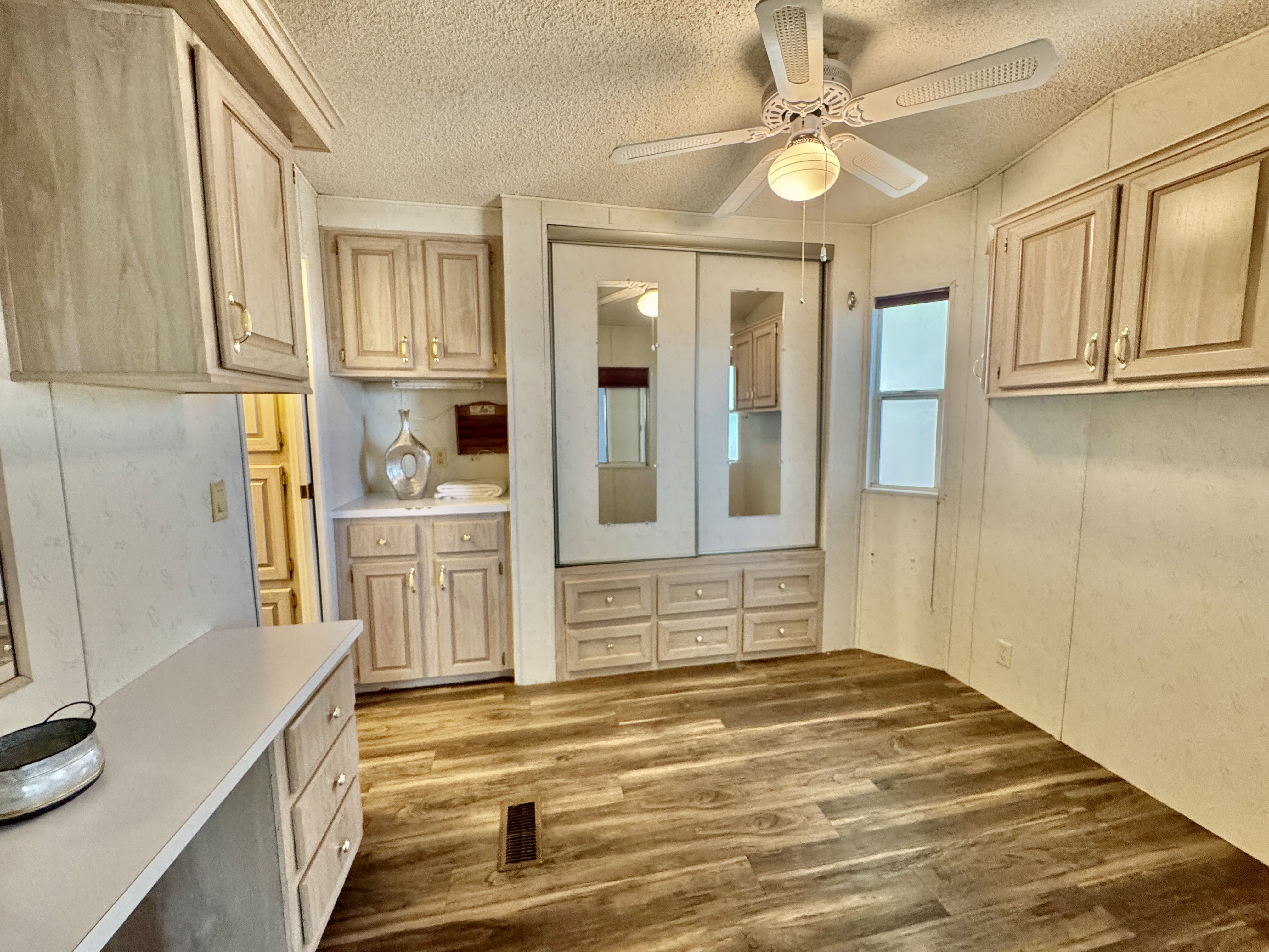 Room featuring wood-finish flooring, a ceiling fan with light fixture, built-in cabinetry, and a mirrored closet with integrated drawers