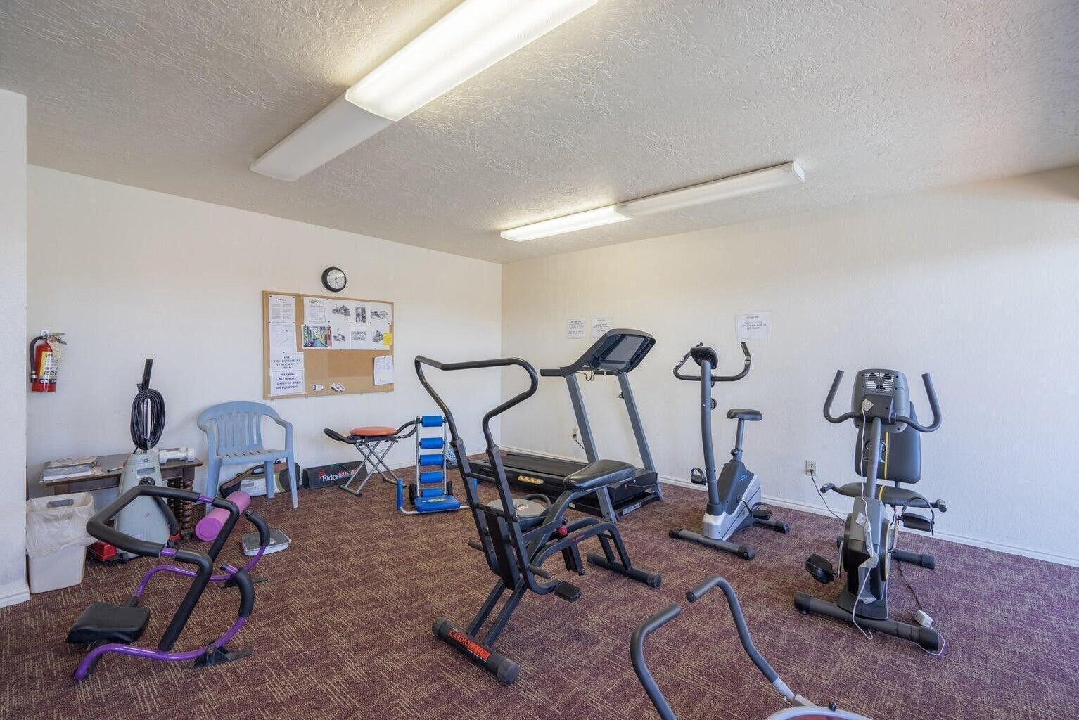 Dedicated fitness room featuring textured carpet, recessed lighting, and a cork board for community notices