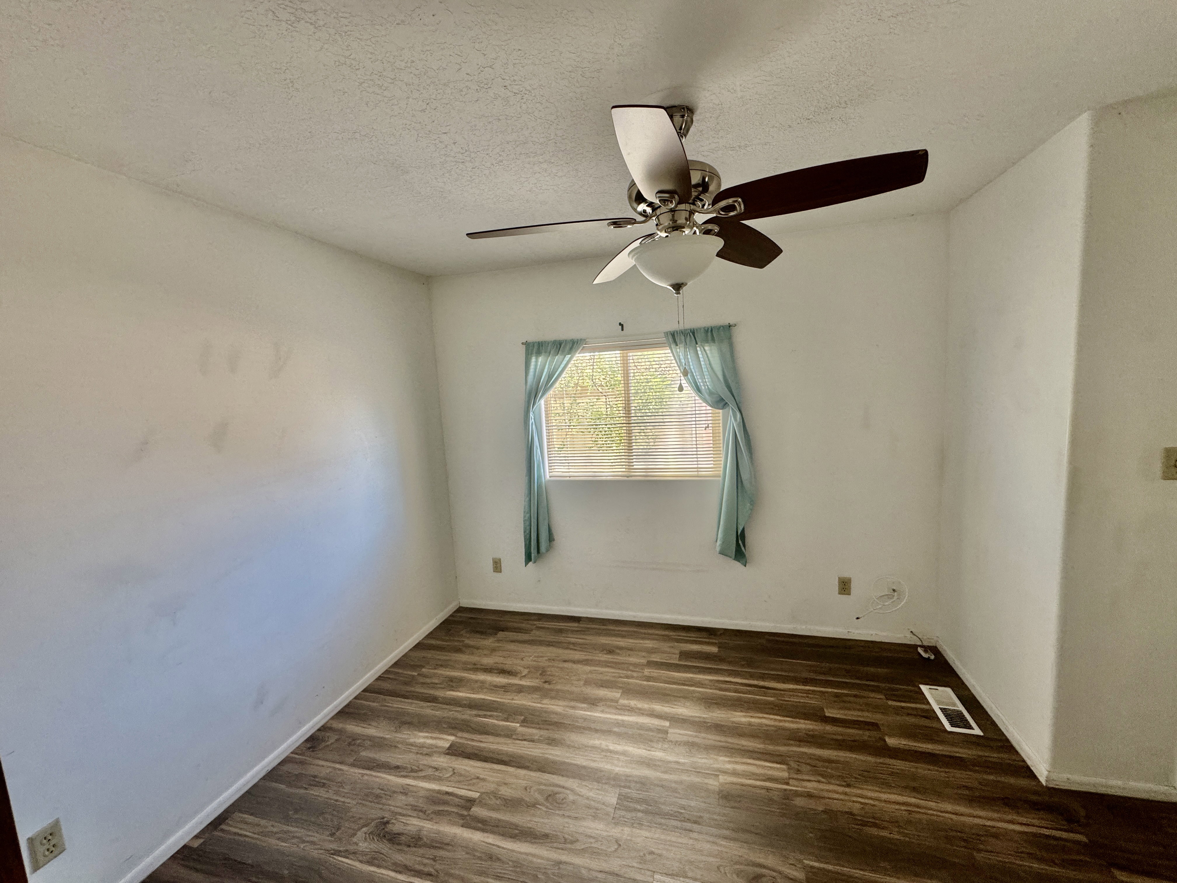 Room featuring wood-finish flooring, a window with light-filtering curtains, and a ceiling fan with integrated lighting