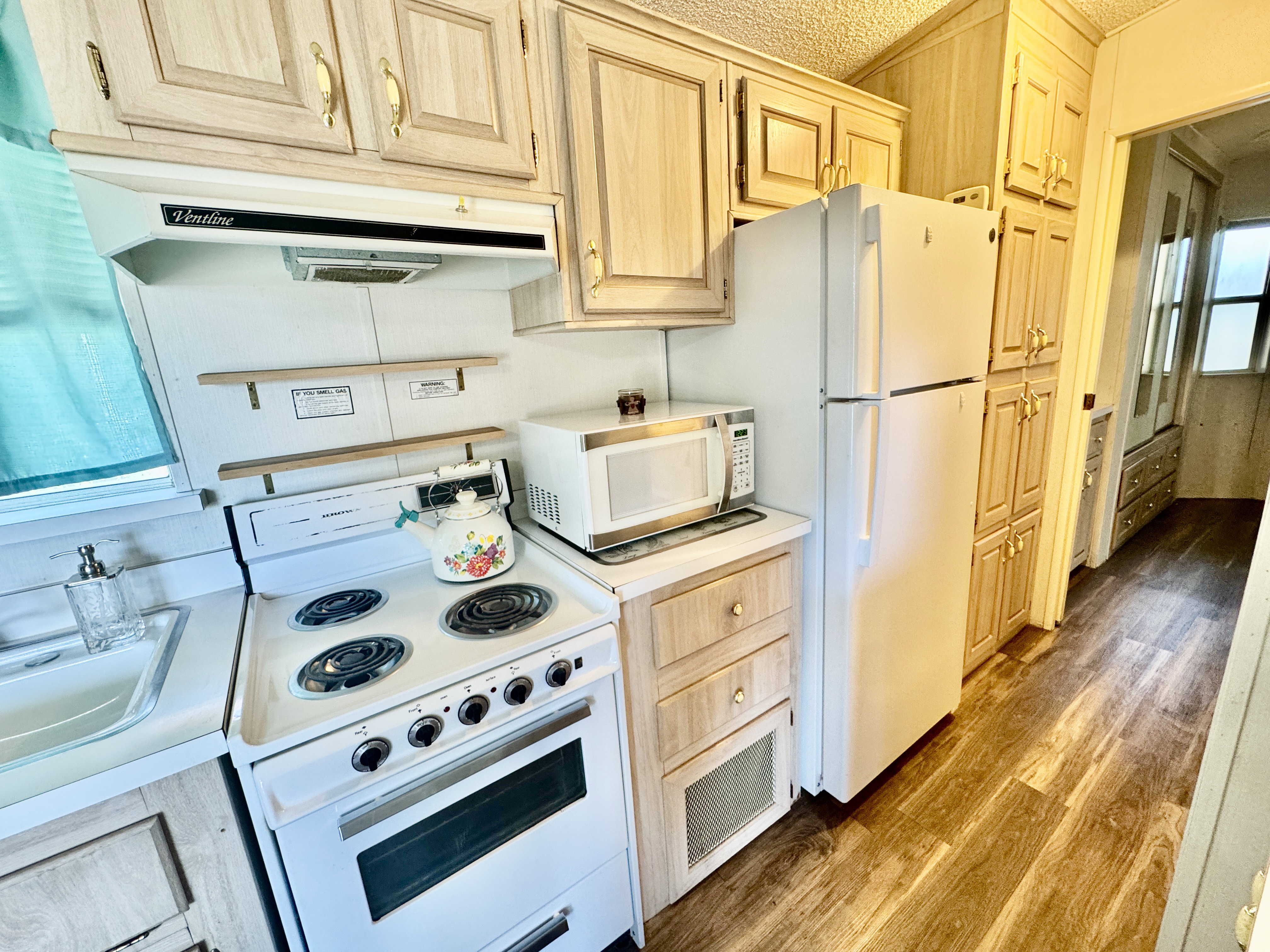 Galley kitchen featuring wood-finish flooring, light wood cabinetry with gold-tone hardware, a white electric range, and a white refrigerator