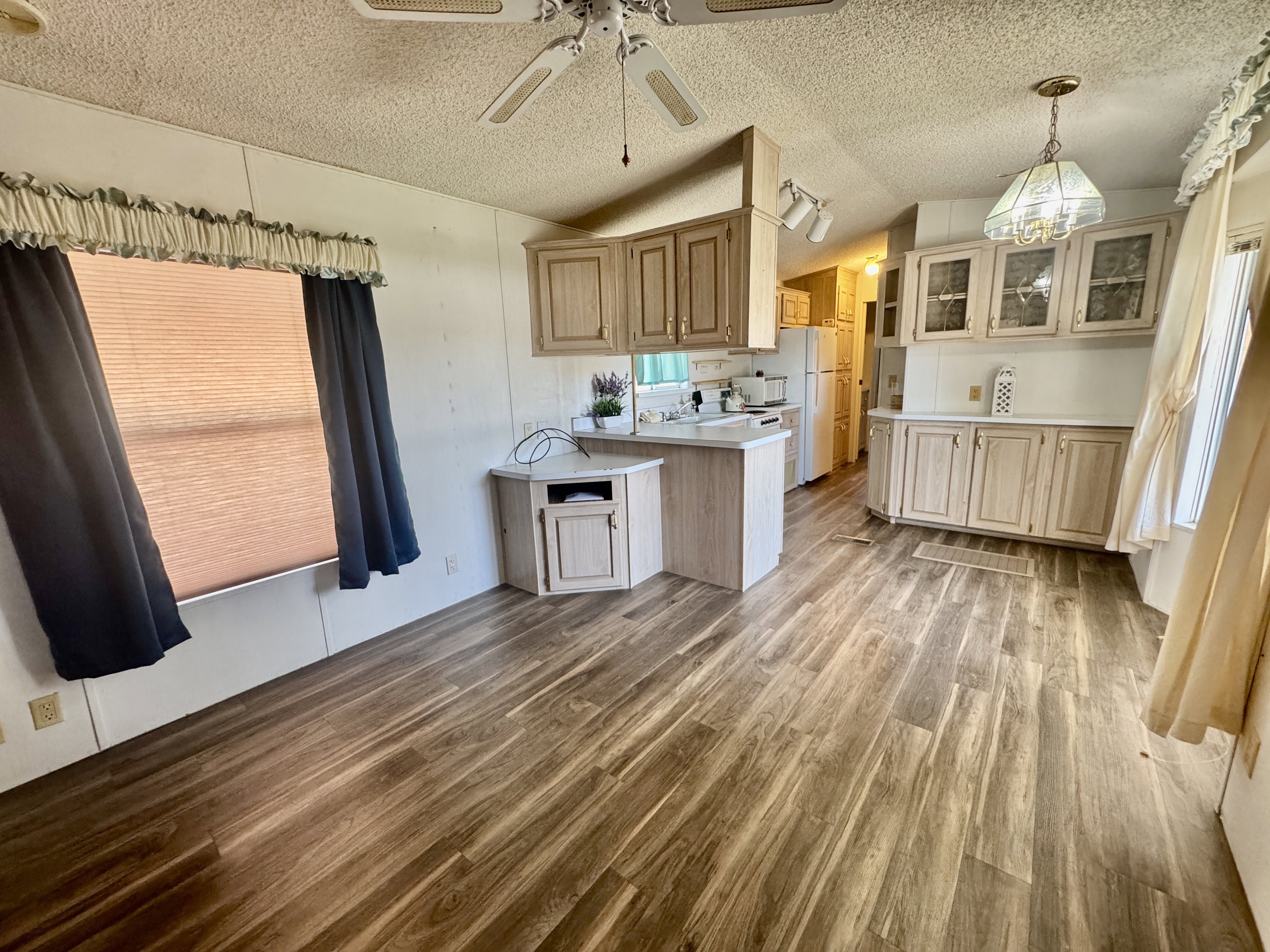Open-concept living space featuring wood-finish flooring, a ceiling fan, and a kitchen area with light-toned cabinetry, white countertops, and white appliances