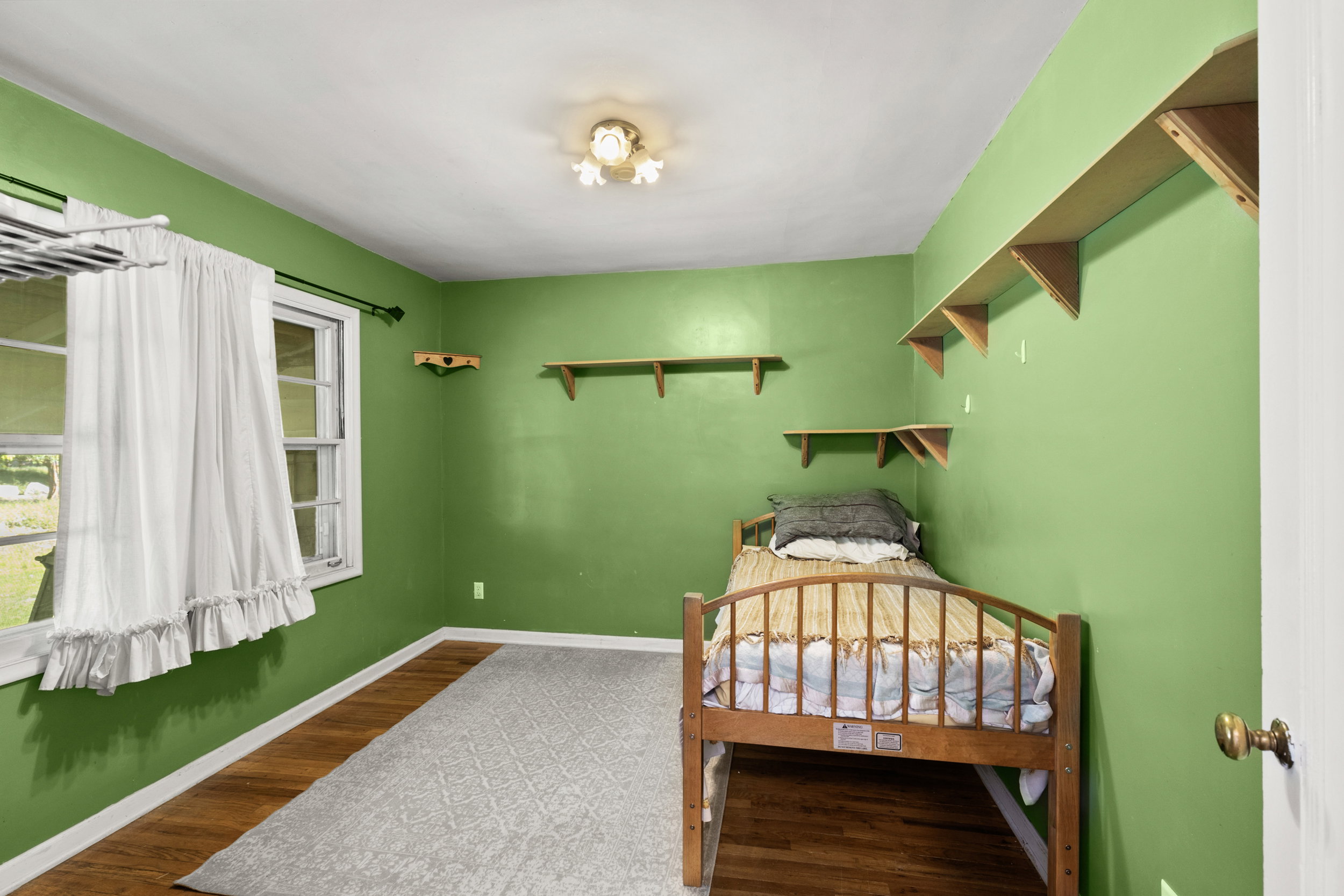 Bright room featuring wood-finish flooring, a white trim baseboard, a window with a white frame, and multiple wall-mounted shelving units