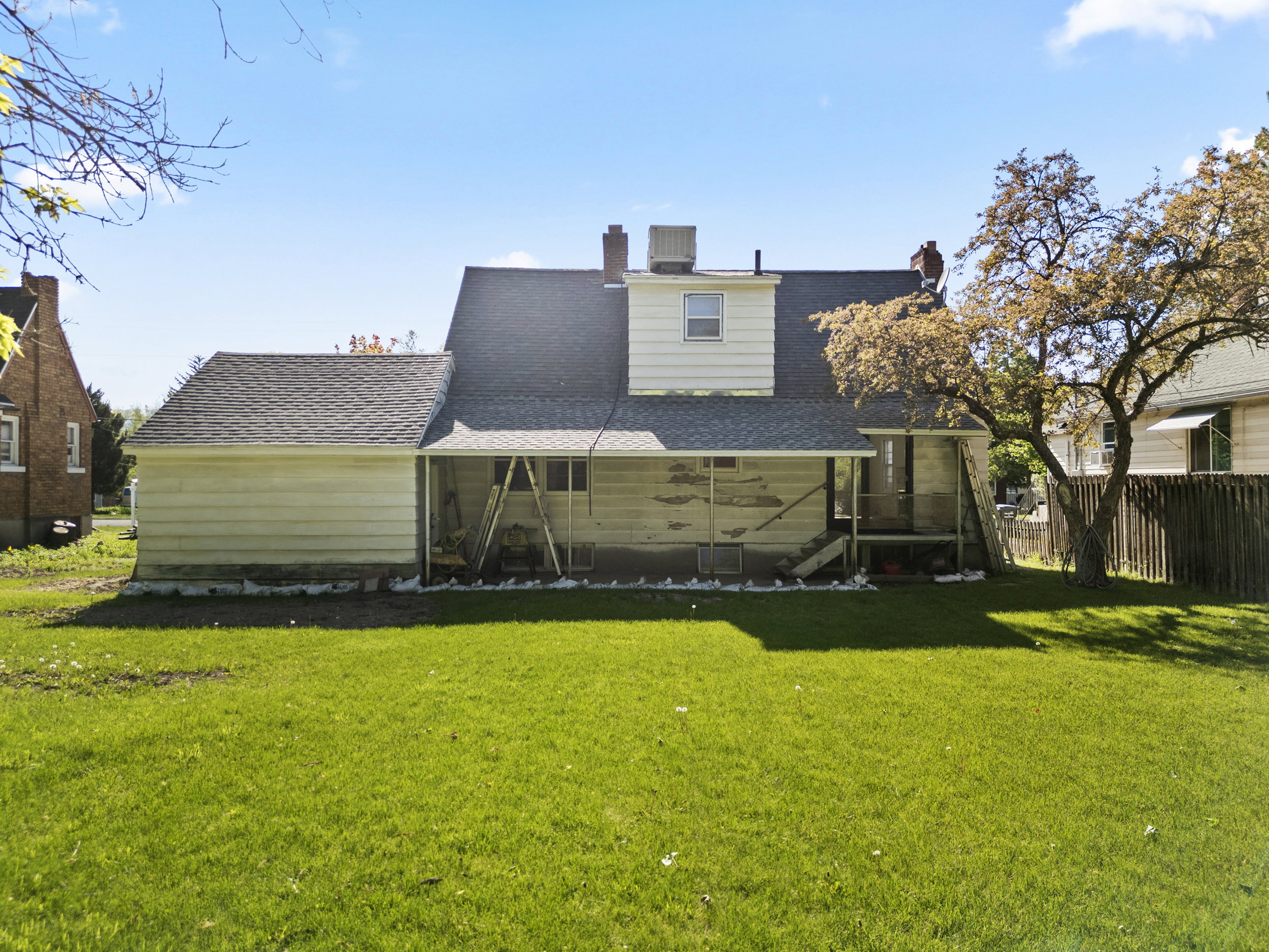 Expansive rear yard featuring a grass lawn, mature tree, and a wooden privacy fence