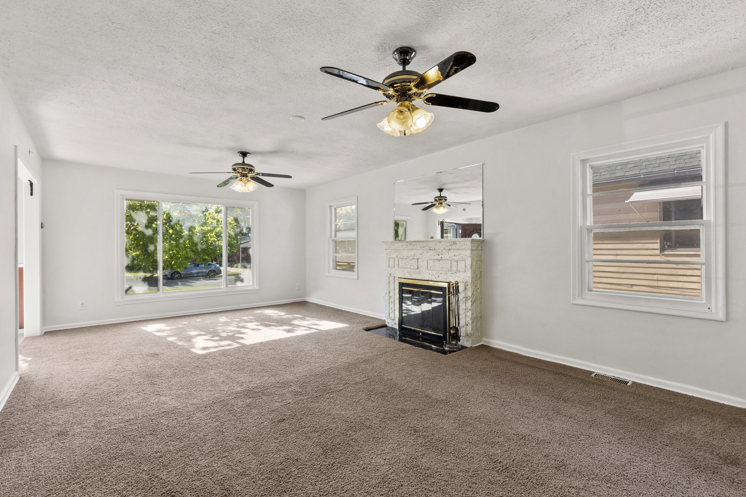 Spacious room featuring a stone fireplace with a black insert, large windows, two ceiling fans, and neutral-toned carpeting