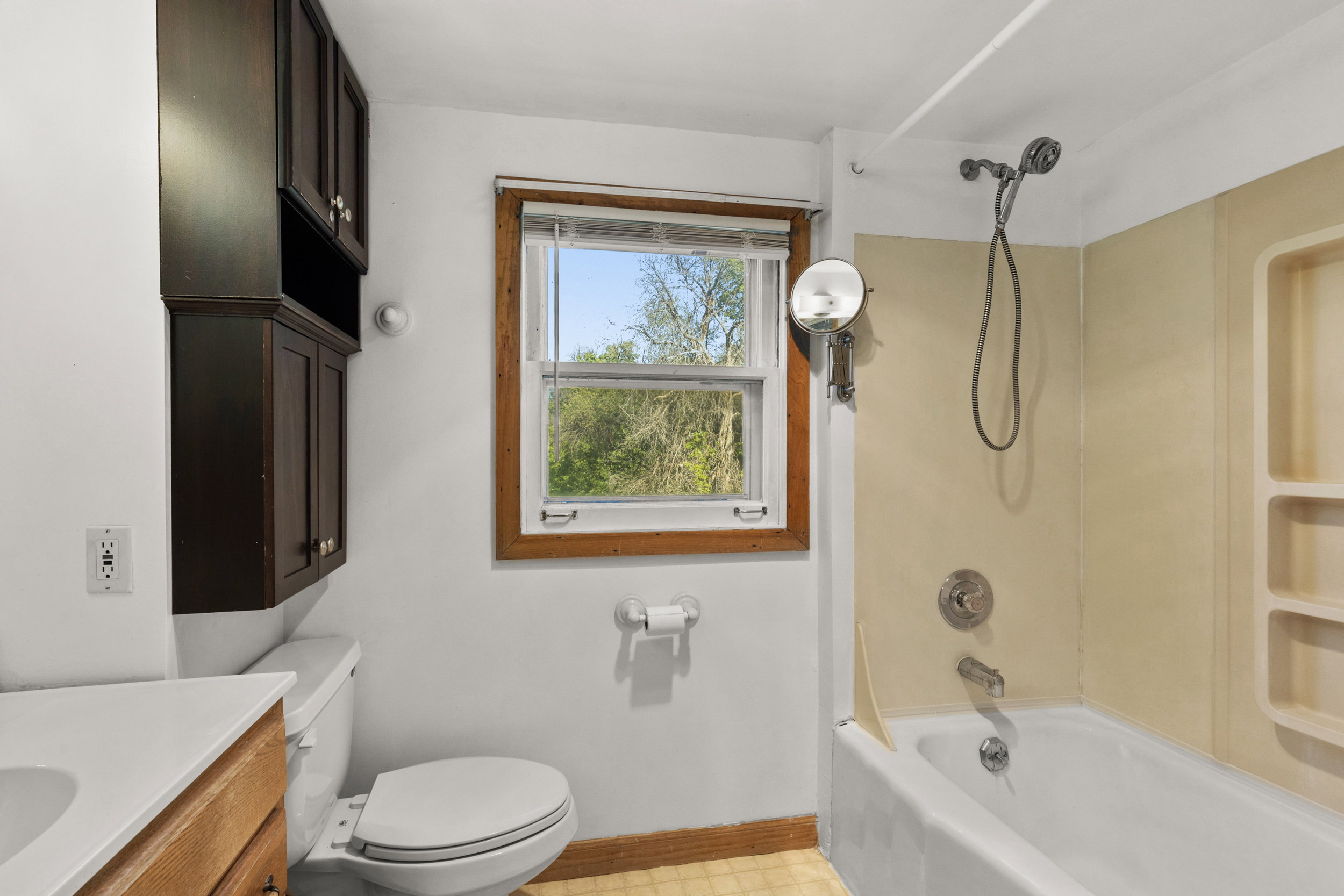 Bathroom featuring a full tub with an integrated shower, built-in storage shelving, dark wood-finish cabinetry, a window with natural light, and a toilet