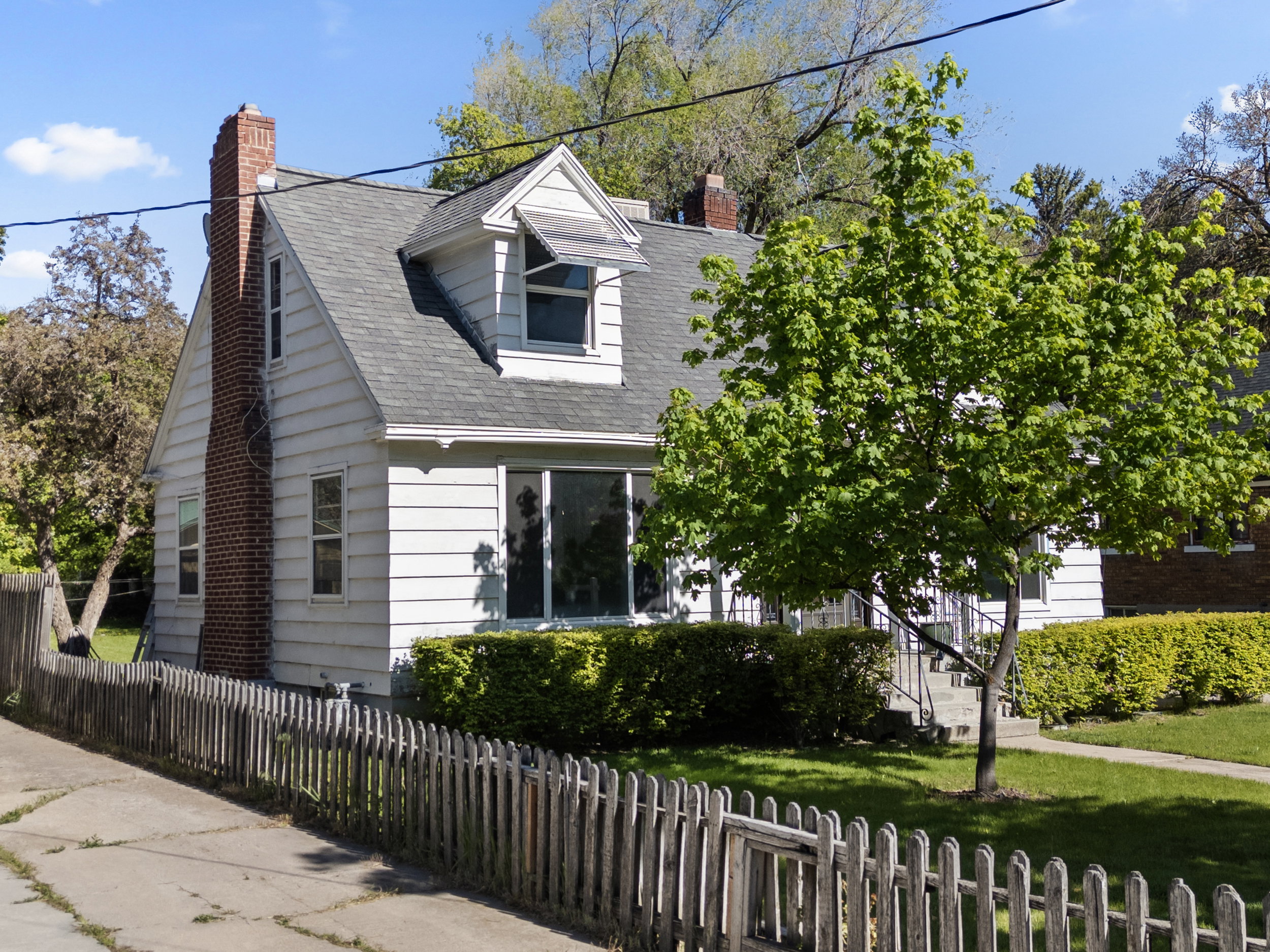 White siding exterior with a prominent brick chimney and a dark shingled roof