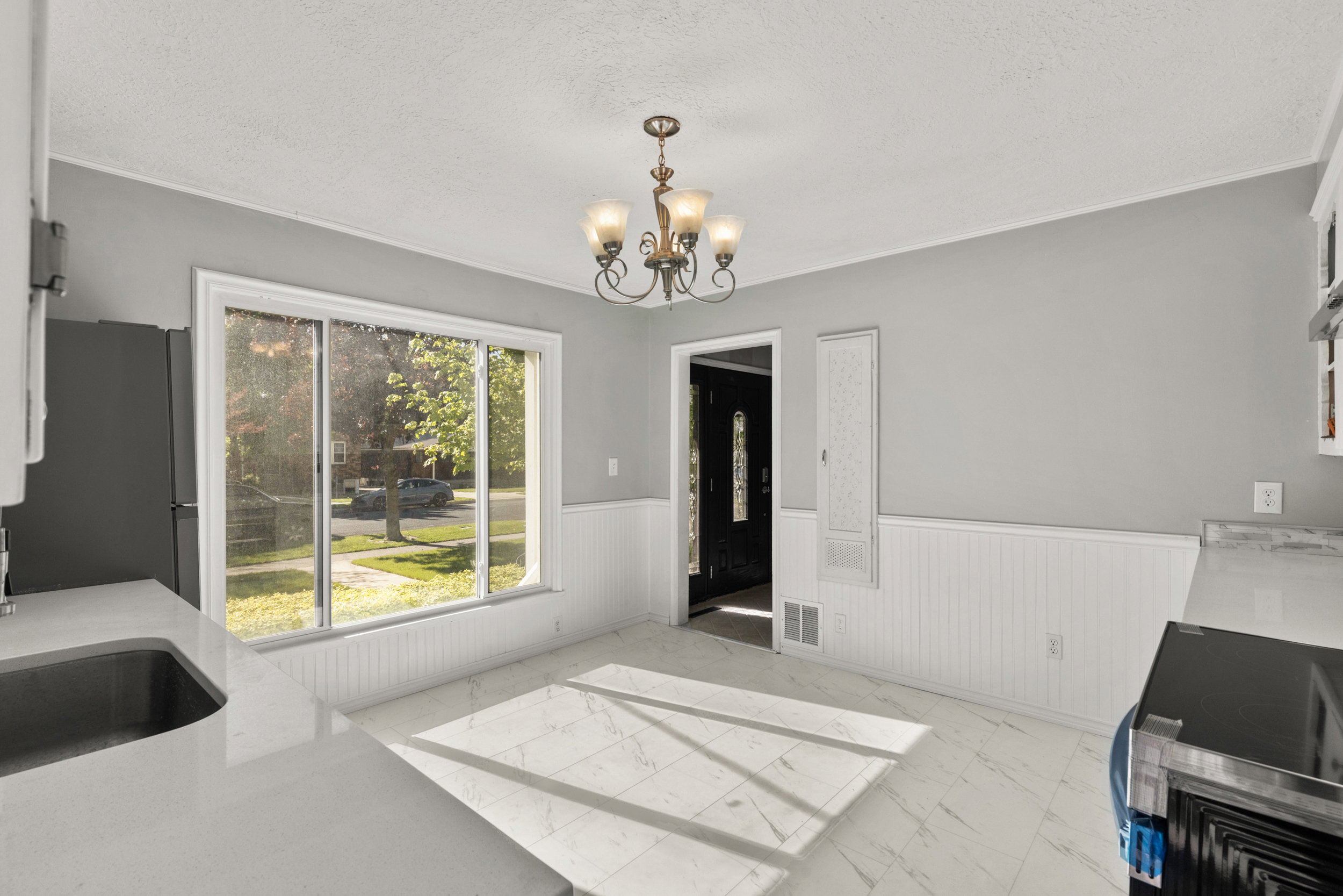 Bright dining area featuring a chandelier, large picture window, white beadboard wainscoting, and white tile flooring