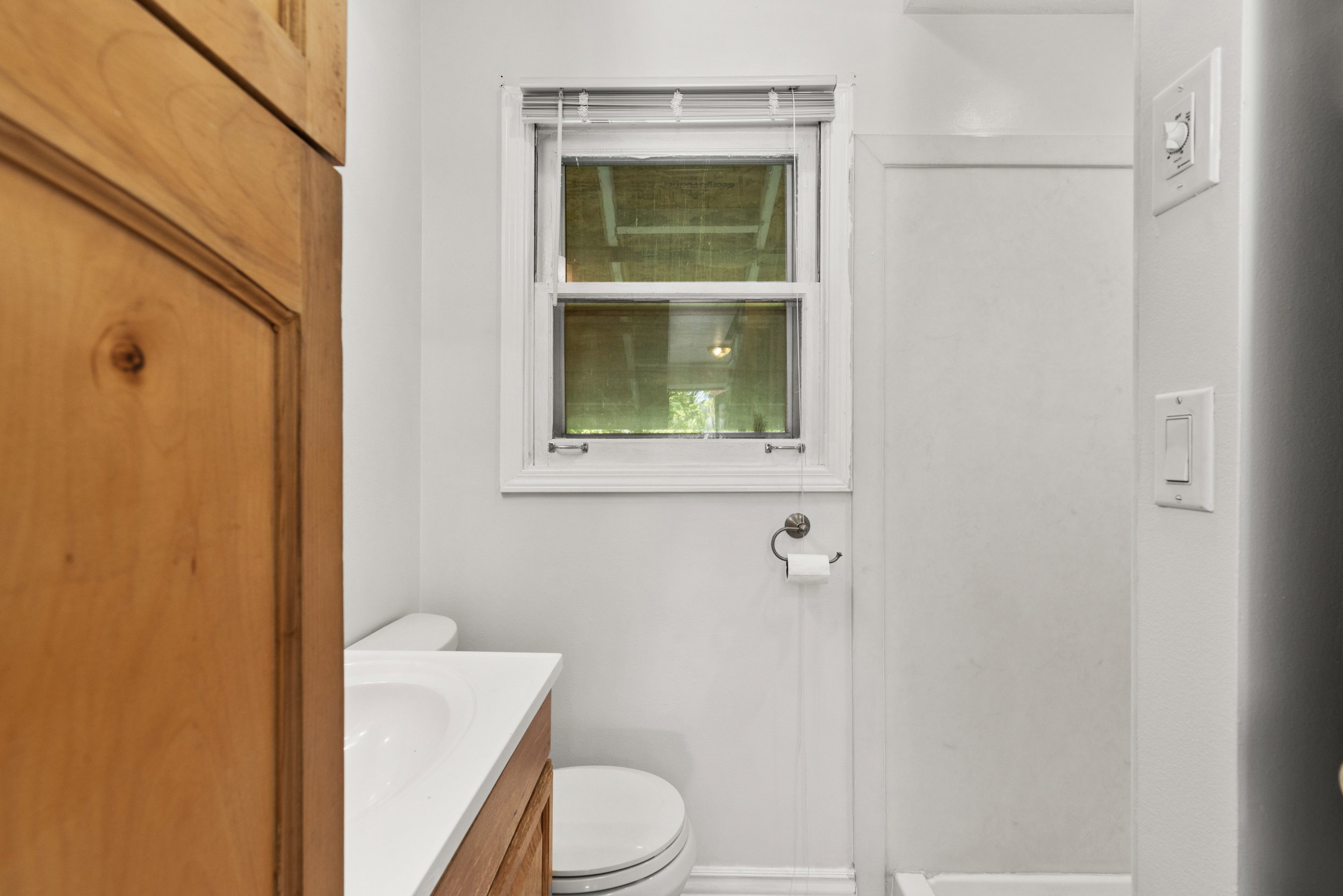 Bathroom featuring a window with blinds, a white vanity with an integrated sink, a toilet, and light wood-finish cabinetry