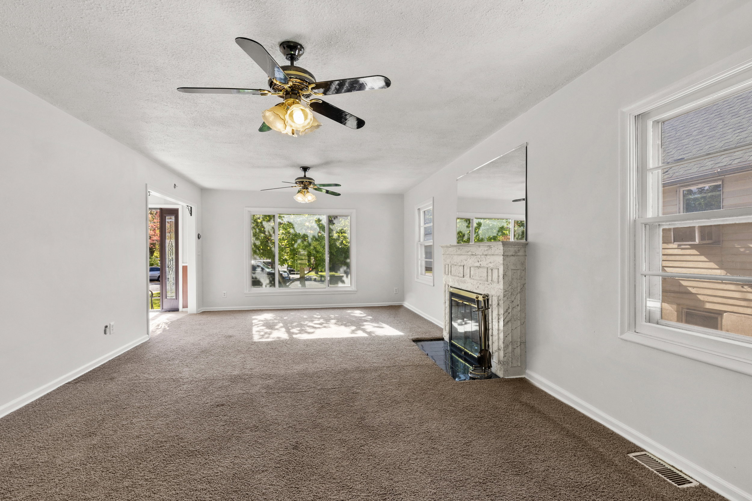 Spacious living area featuring a stone fireplace, multiple windows, plush carpet, and two ceiling fans