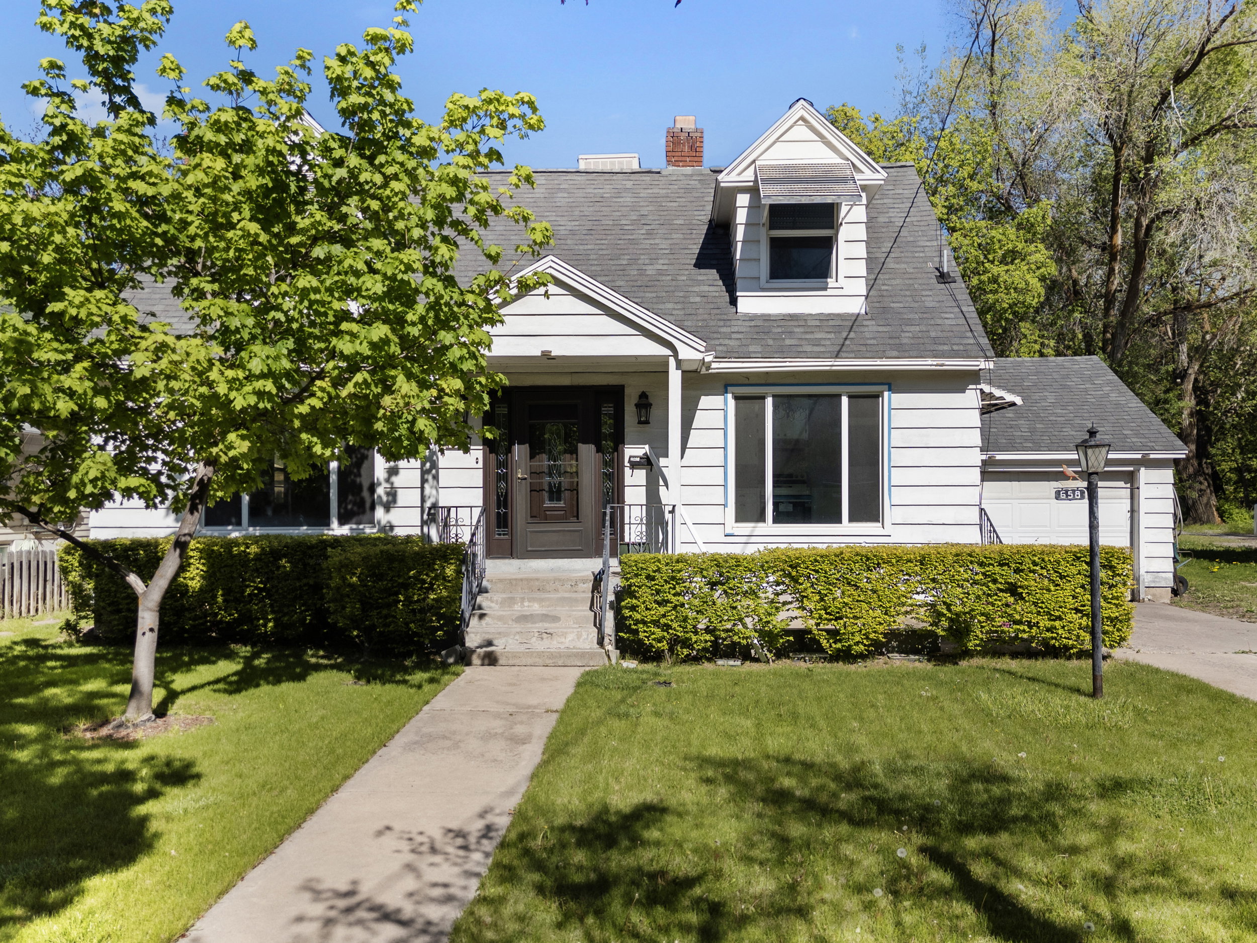 White siding residence featuring a dark front door, a dormer window, and an attached garage