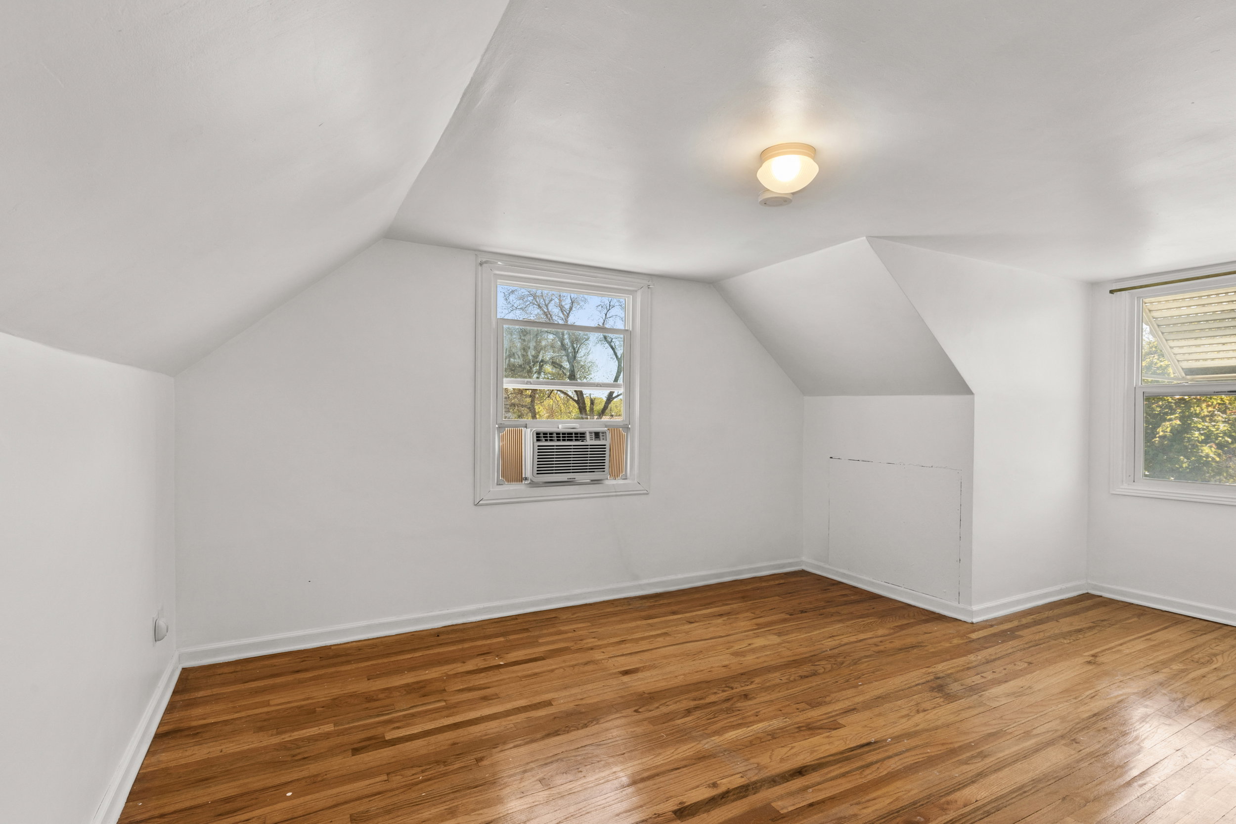 Room featuring wood-finish flooring, two windows, sloped ceilings, a ceiling-mounted light fixture, and white painted walls