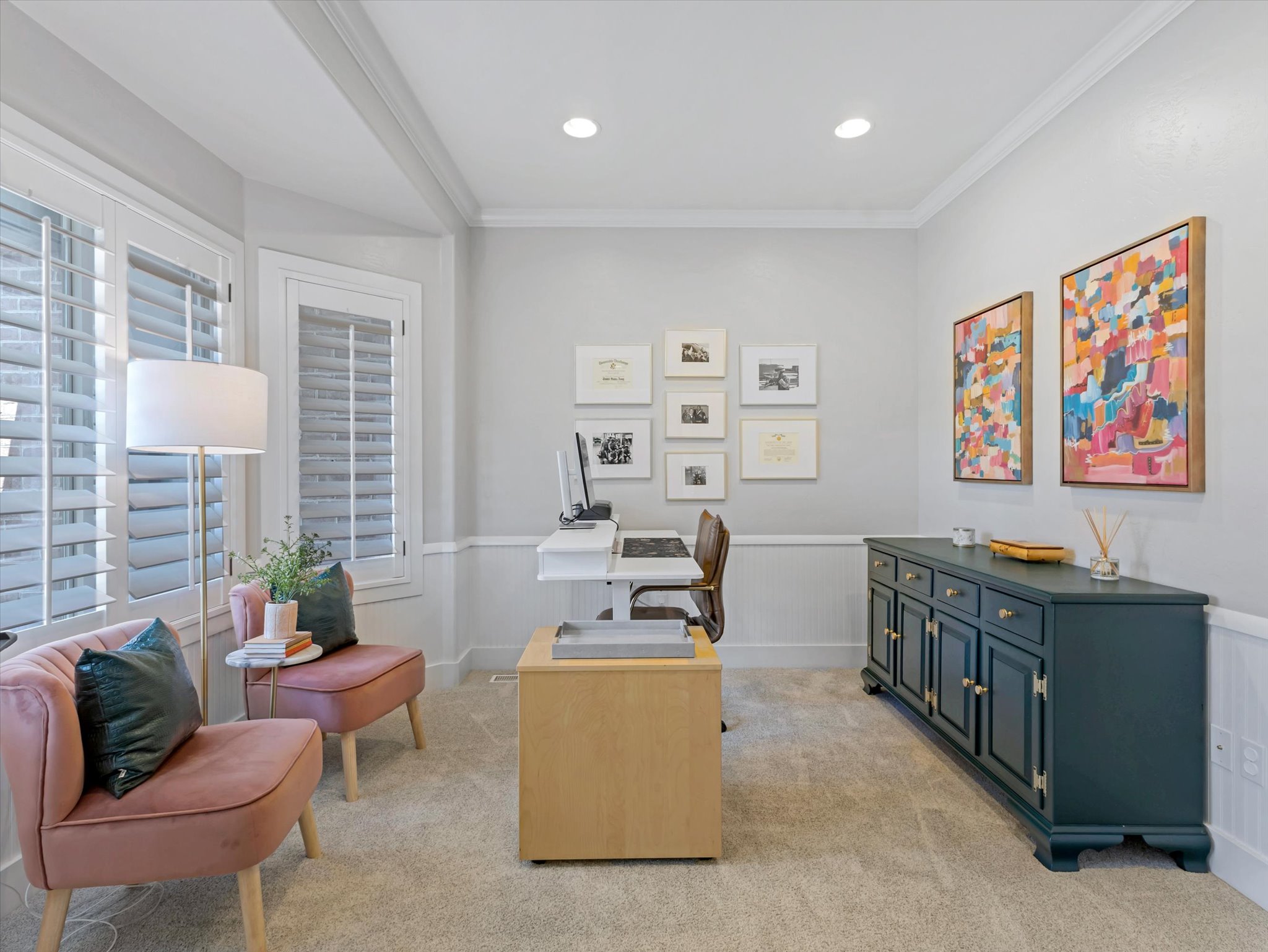 Recessed lighting illuminates this versatile room featuring plantation shutters, crown molding, and wainscoting
