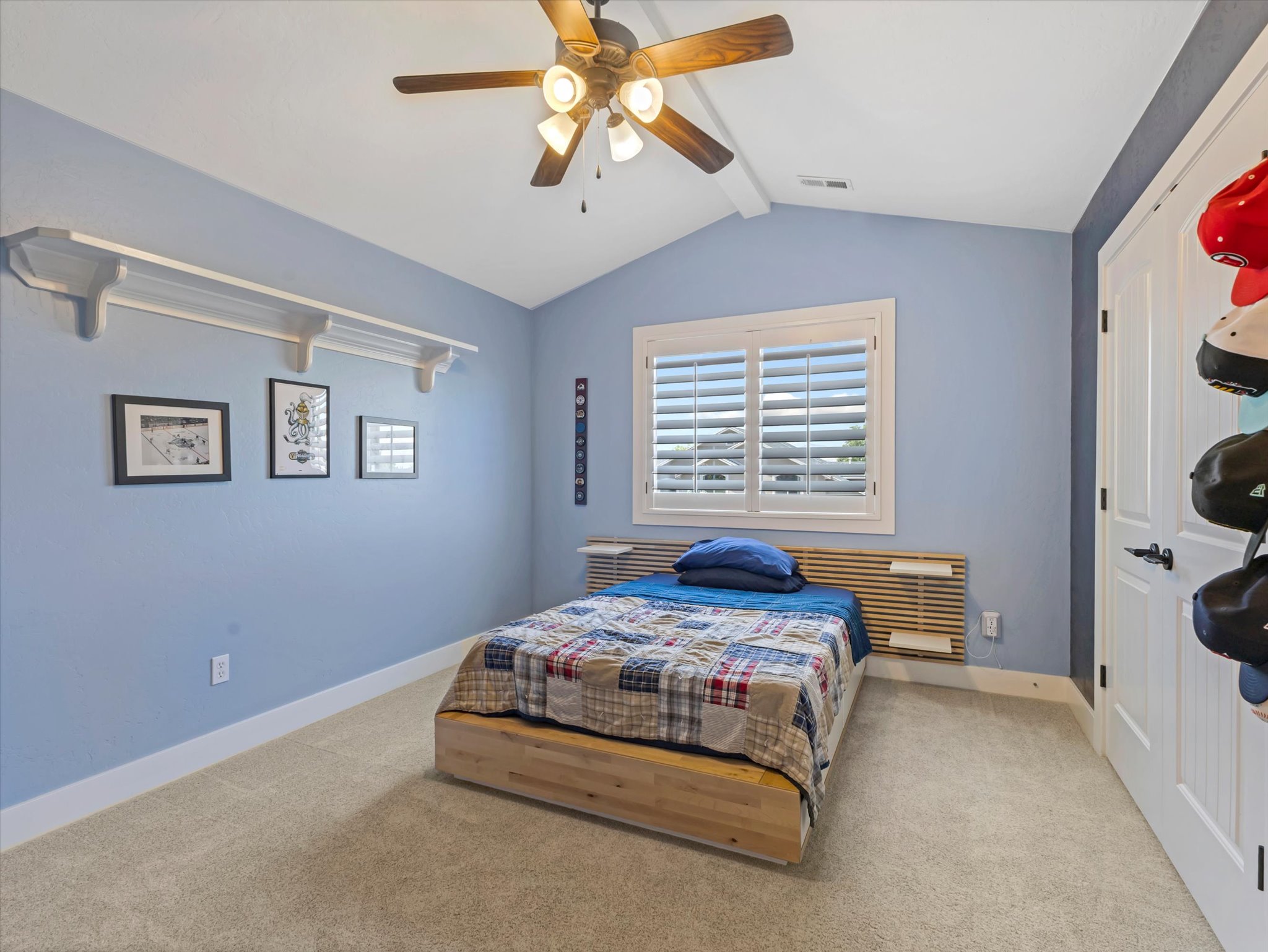 Vaulted ceiling with a ceiling fan, window with plantation shutters, light-toned carpet flooring, white baseboards, and a white paneled door