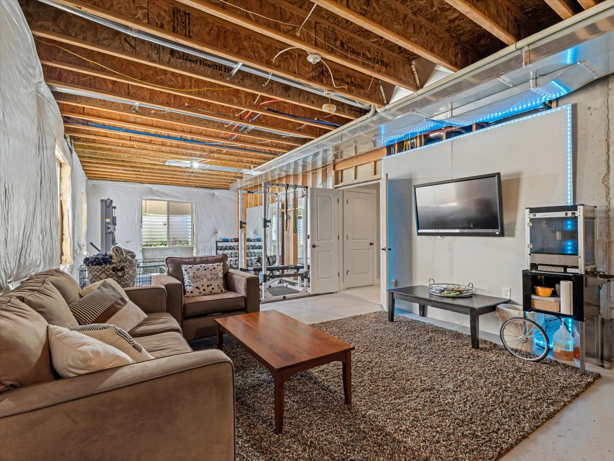 Unfinished lower level with exposed ceiling joists and ductwork, featuring a recessed window, white paneled walls, and double white doors