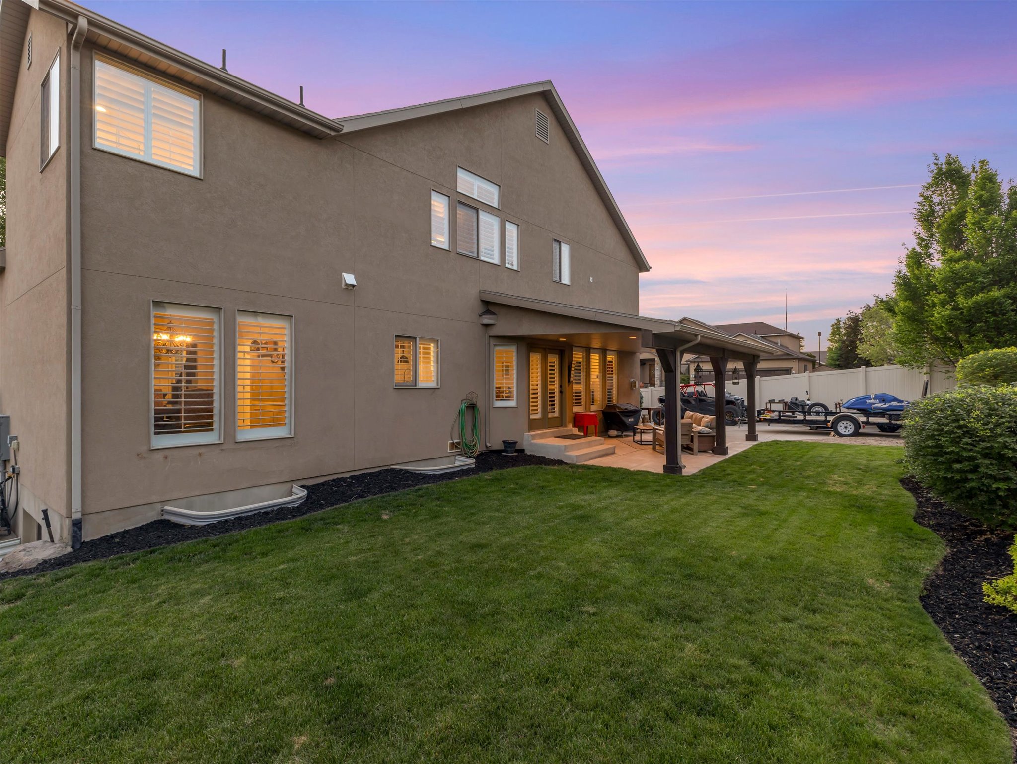 Expansive backyard featuring a manicured lawn, a covered patio, and a pergola with structural columns