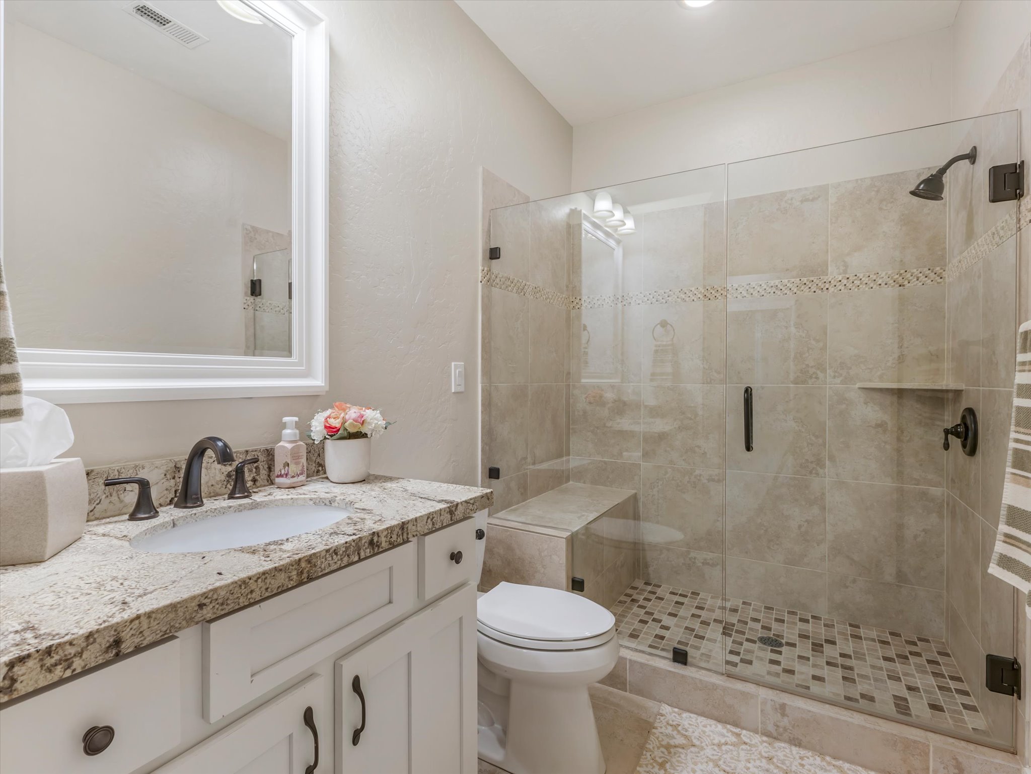 Bathroom featuring a granite-topped vanity with undermount sink, oil-rubbed bronze fixtures, and white cabinetry