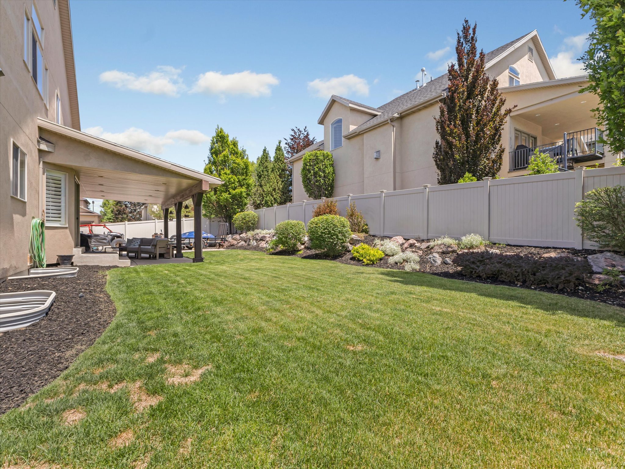 Spacious backyard featuring a covered patio, a large lawn area, a retaining wall with rock landscaping, and a privacy fence