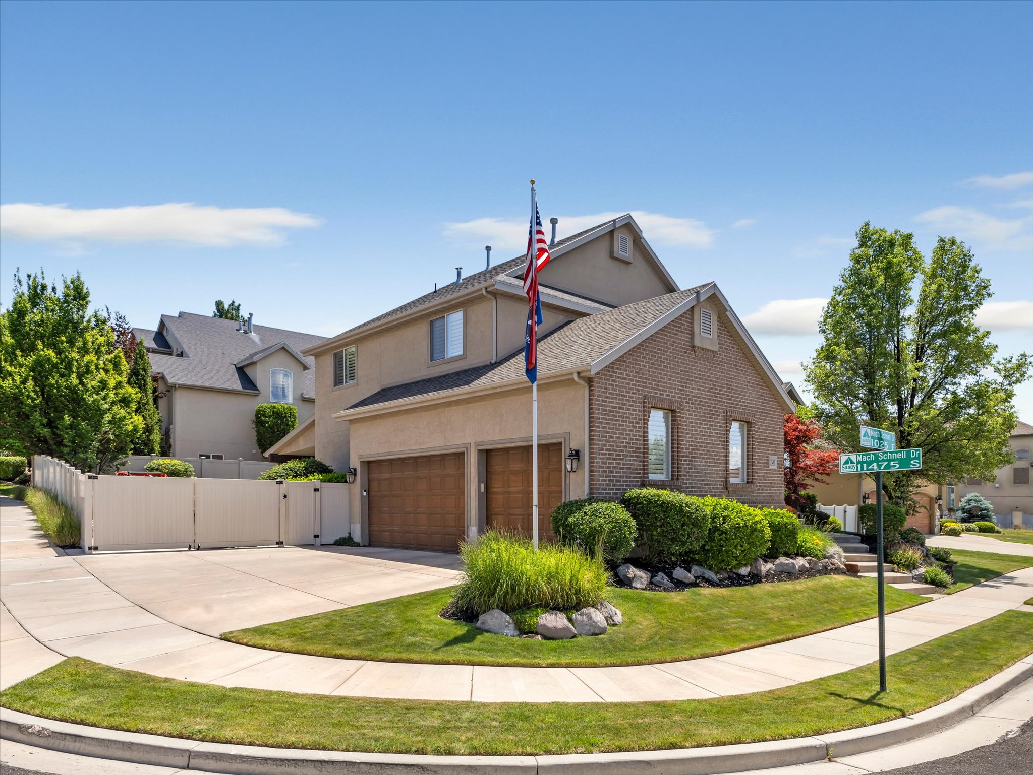 Two-story residence featuring a brick and stucco exterior, a two-car garage with wood-finish doors, and a corner lot with mature landscaping