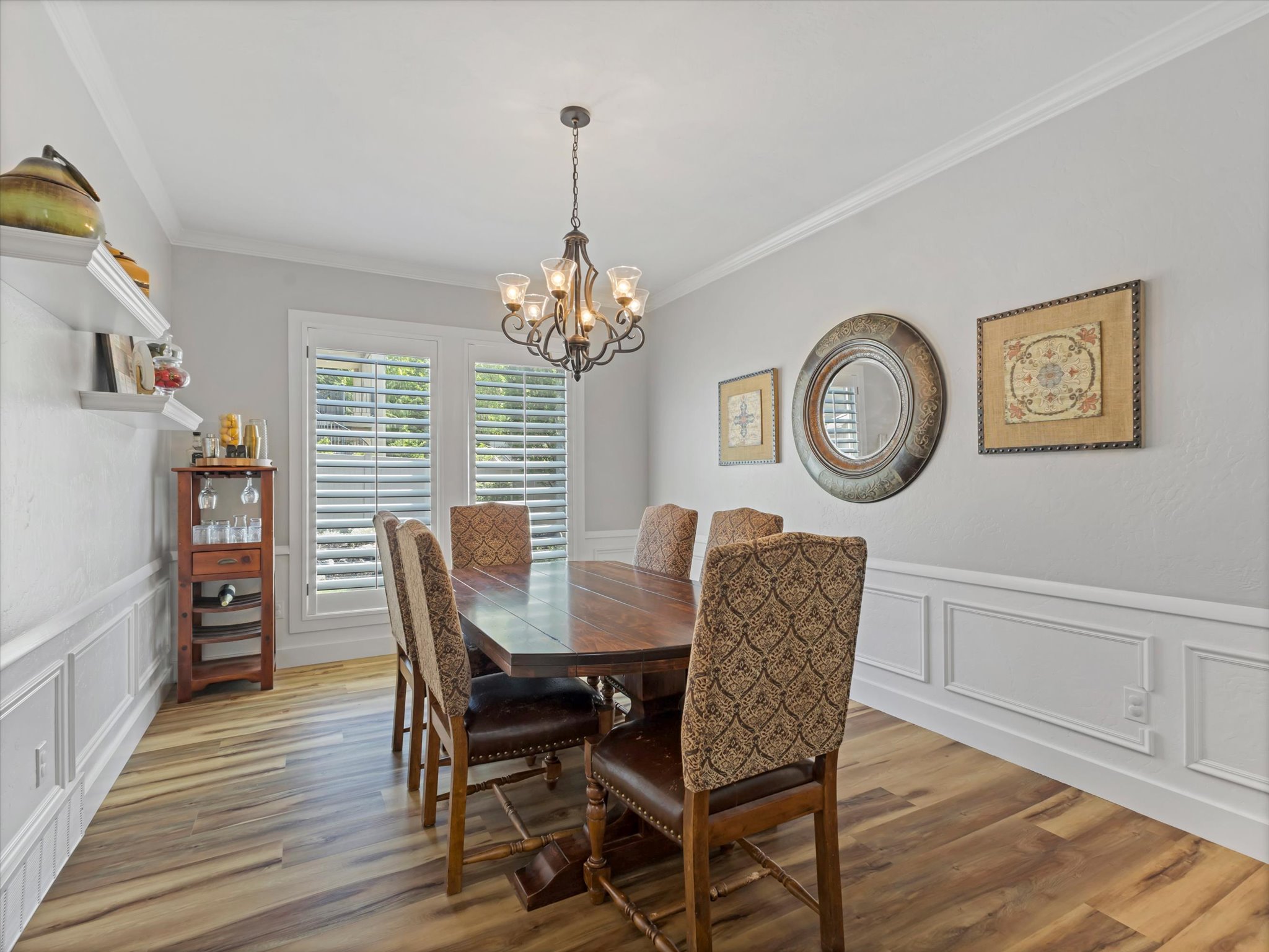Dining area featuring wood-finish flooring, wainscoting, crown molding, and plantation shutters