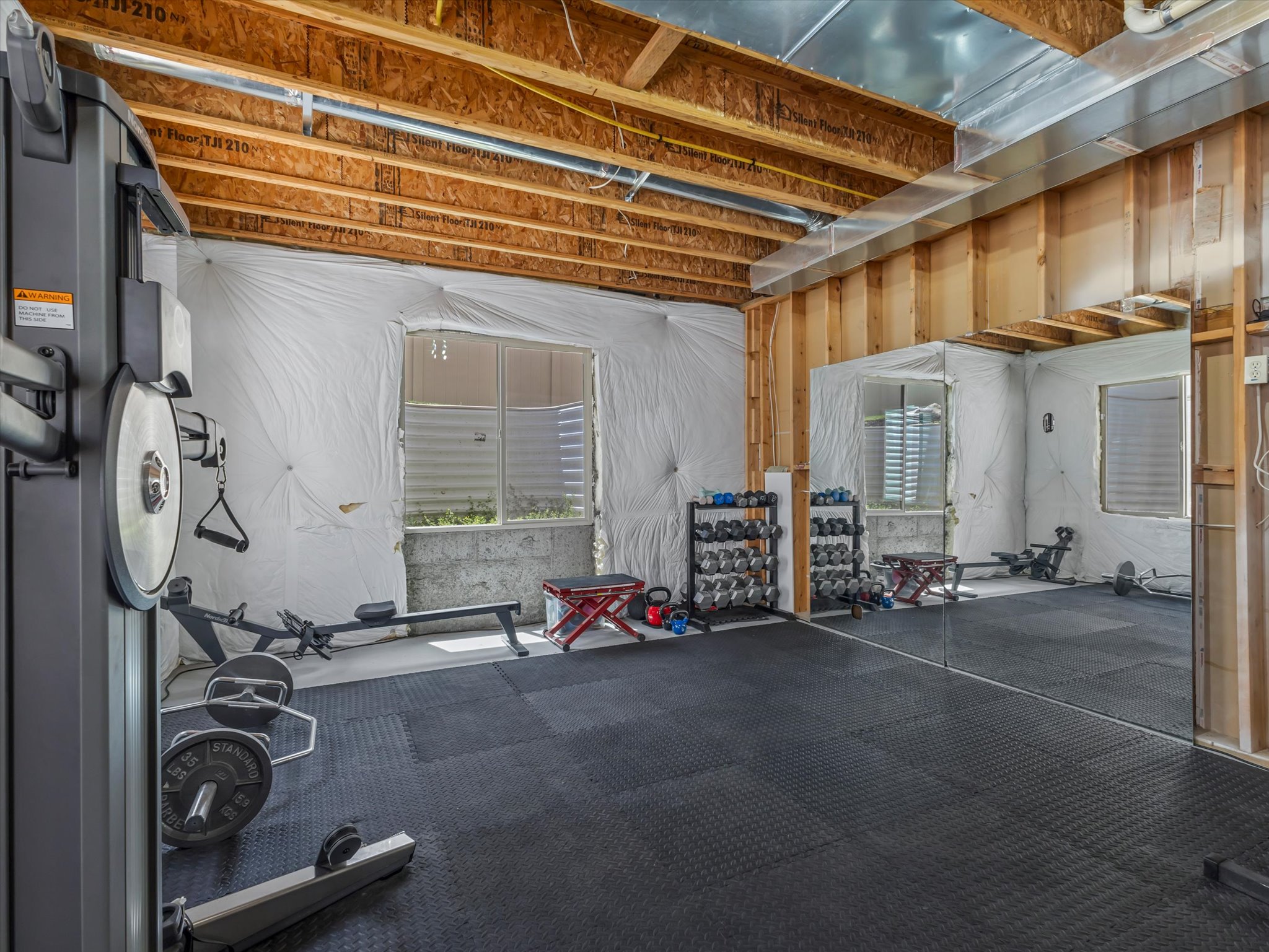 Unfinished basement space featuring exposed wooden joists, visible insulation, and a concrete foundation