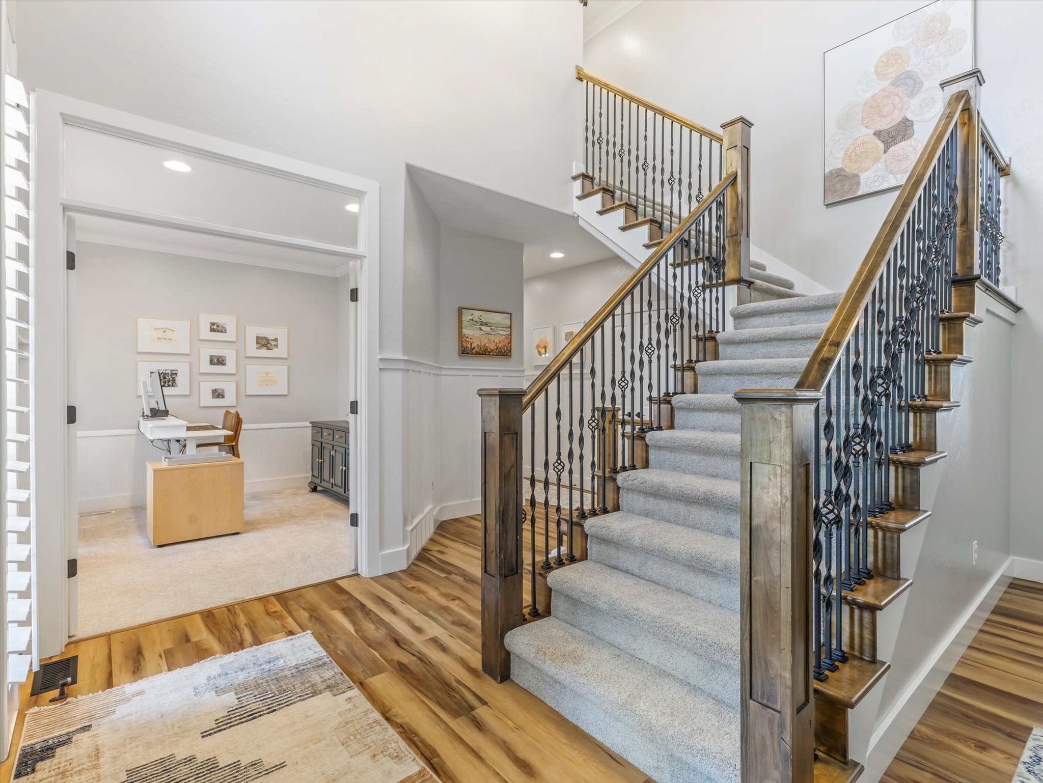 Grand entryway featuring wood-finish flooring, a carpeted staircase with ornate wrought iron and wood balusters, and wainscoting
