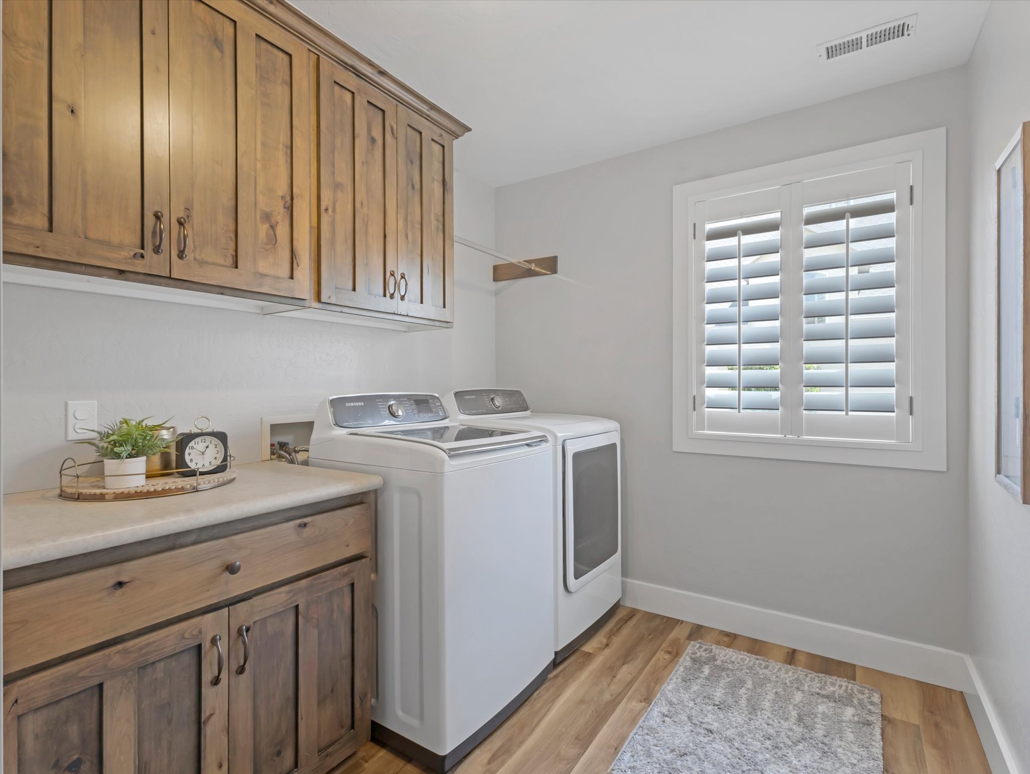 Laundry area featuring wood-finish flooring, built-in wooden cabinetry, a light-colored countertop, and a window with white plantation shutters