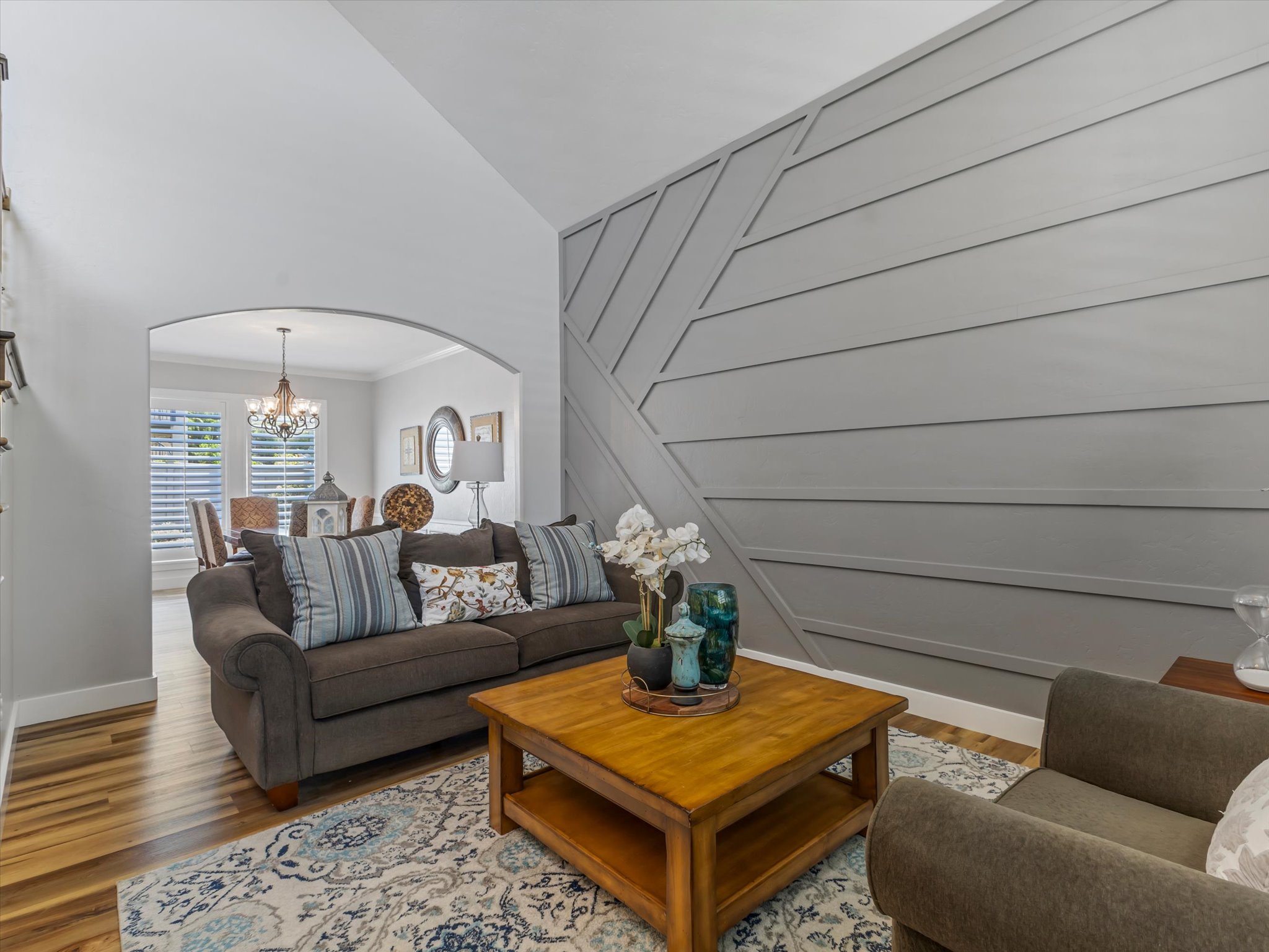 Living area featuring an accent wall with geometric paneling, wood-finish flooring, and an arched entryway