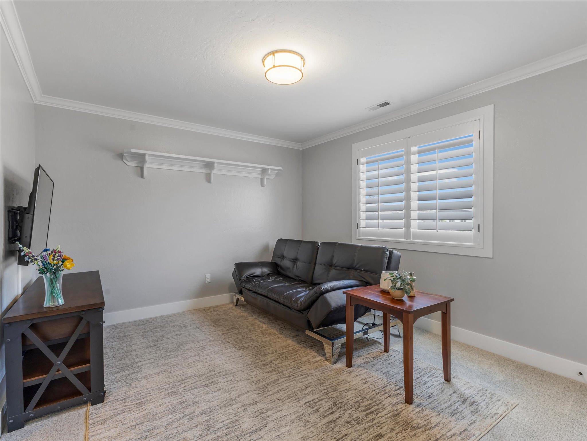 Bright room featuring a window with white plantation shutters, crown molding, and a built-in wall shelf