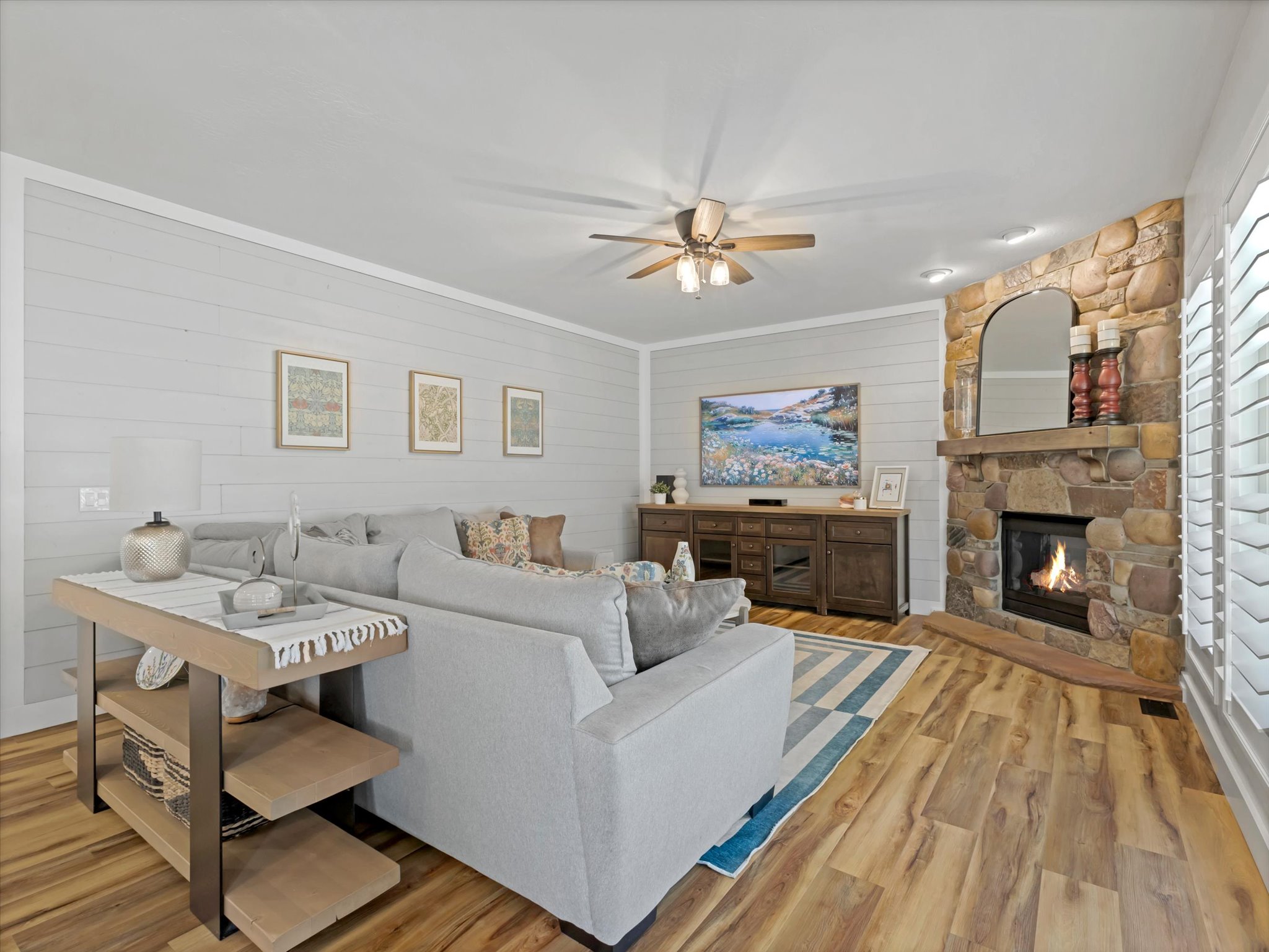 Living area featuring wood-finish flooring, a stone-clad fireplace with a wood mantle, and white horizontal plank walls