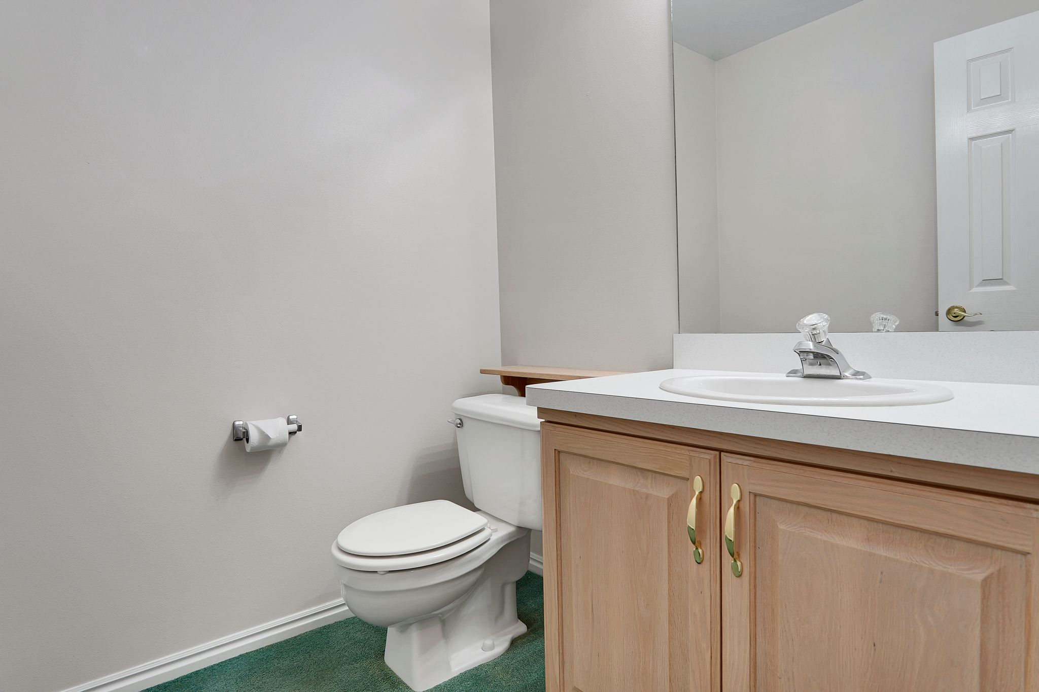 Bathroom featuring a light wood-finish vanity with a white countertop and integrated sink, a large wall-mounted mirror, a standard toilet, and green-hued carpet flooring