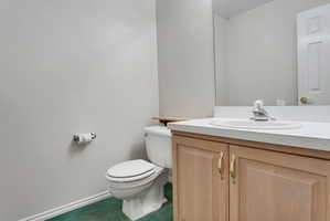 Bathroom featuring a light wood-finish vanity with a white countertop and integrated sink, a large wall-mounted mirror, a standard toilet, and green-hued carpet flooring
