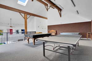 Spacious loft area featuring vaulted ceilings with exposed wood beams, skylight, and wall-to-wall carpeting