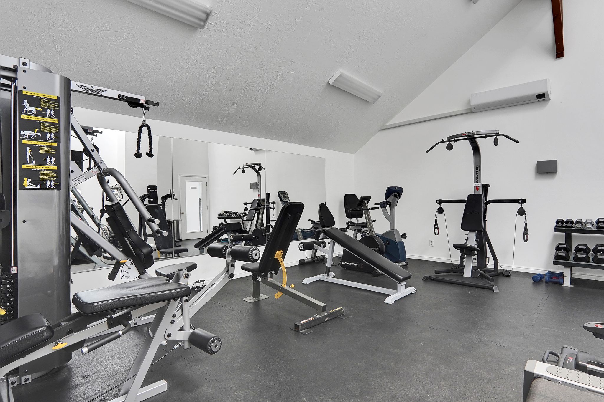 Dedicated fitness area featuring rubber flooring, mirrored wall, and vaulted ceiling